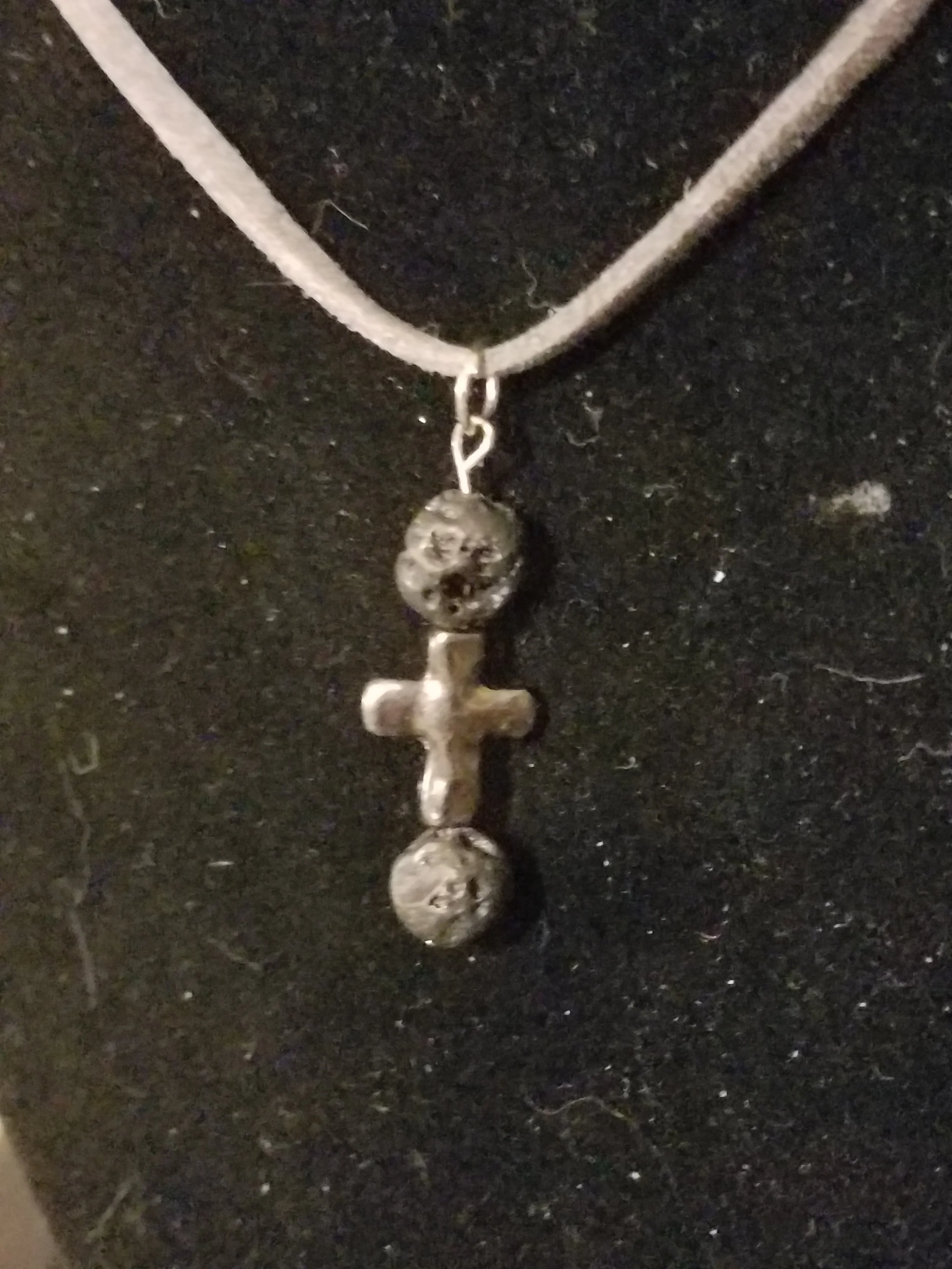 Silver necklace with a cross pendant, featuring two circular gemstones, on a black background.