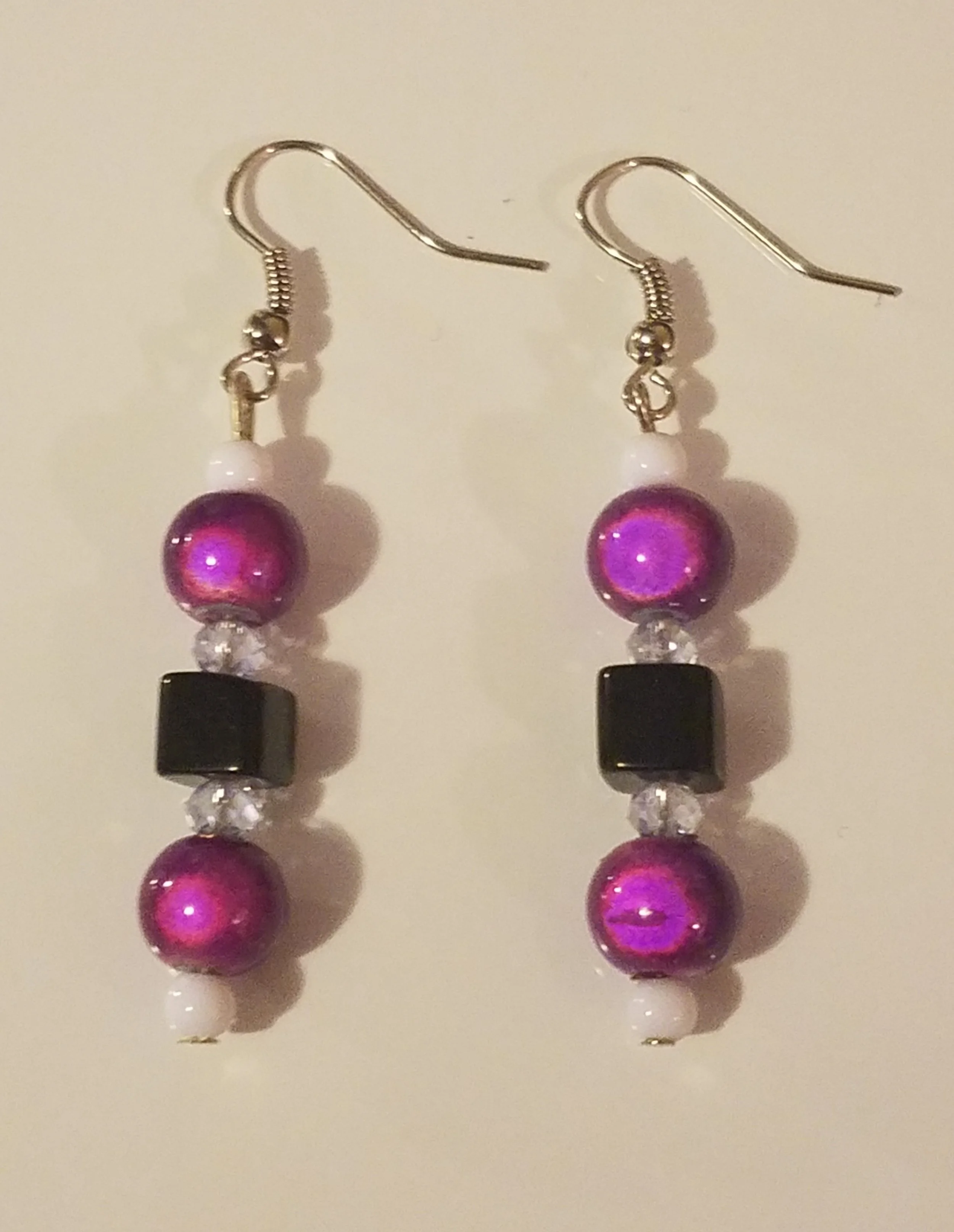 Pair of dangling earrings with purple beads, black cube beads, and clear beads, hanging from silver hooks.