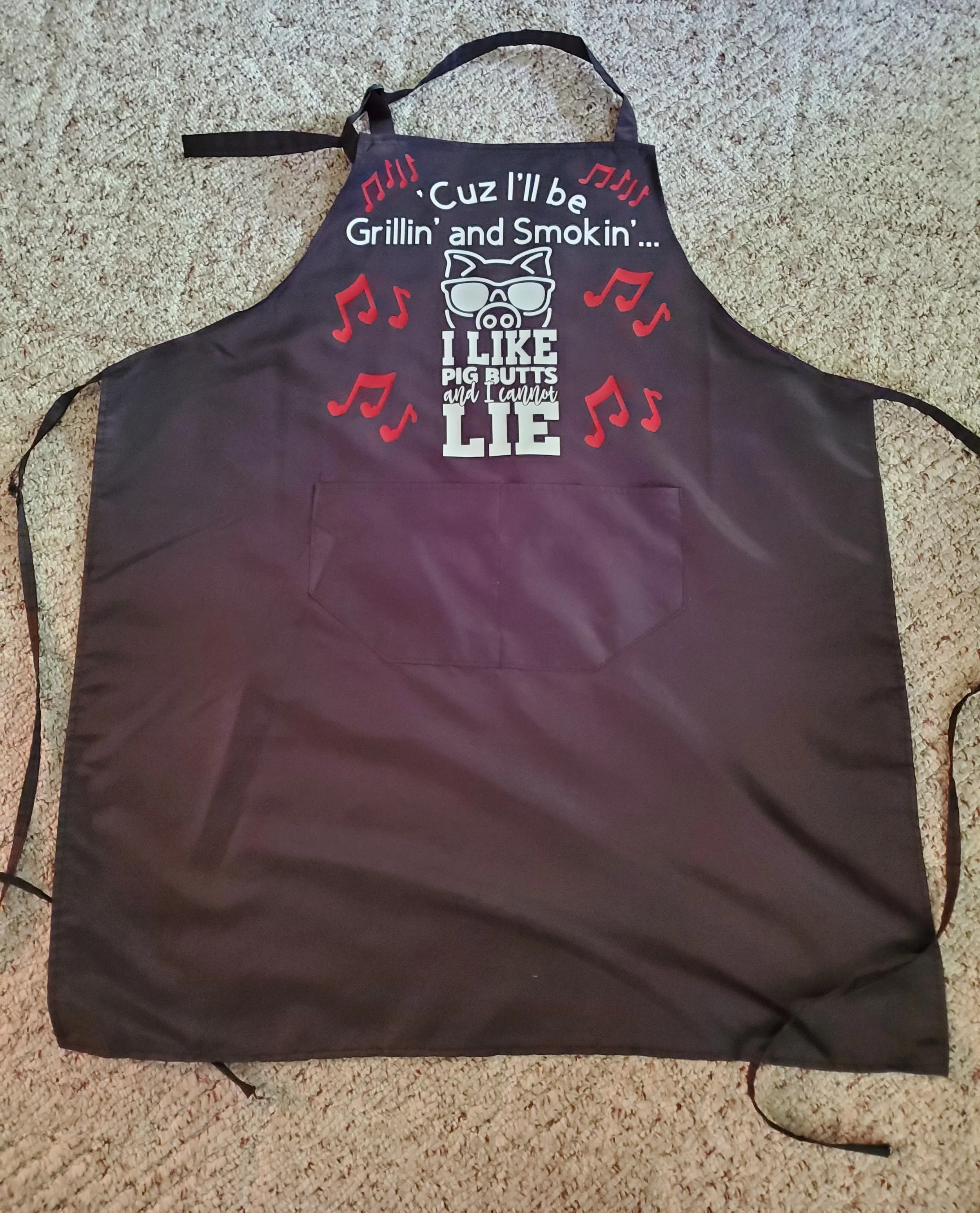 Black apron with a pig wearing sunglasses and the text 'Cuz I'll be Grillin' and Smokin'... I LIKE PIG BUTTS and I can't LIE' surrounded by red musical notes.