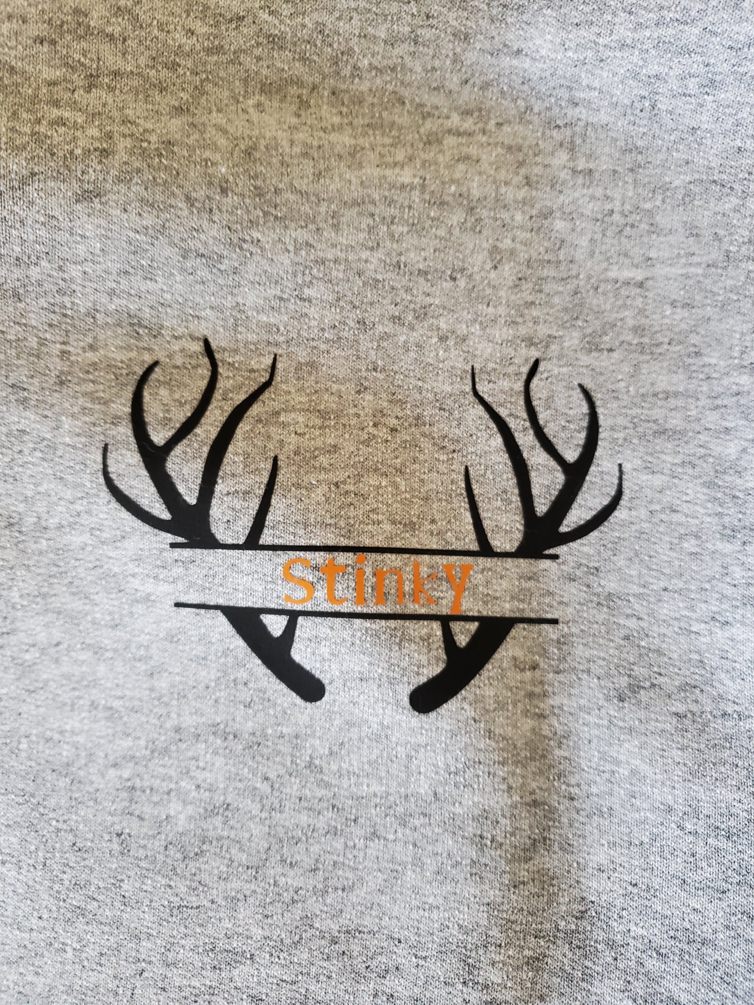 Gray fabric with a black graphic of a deer antler set and the word "Stinky" in orange over the antlers.