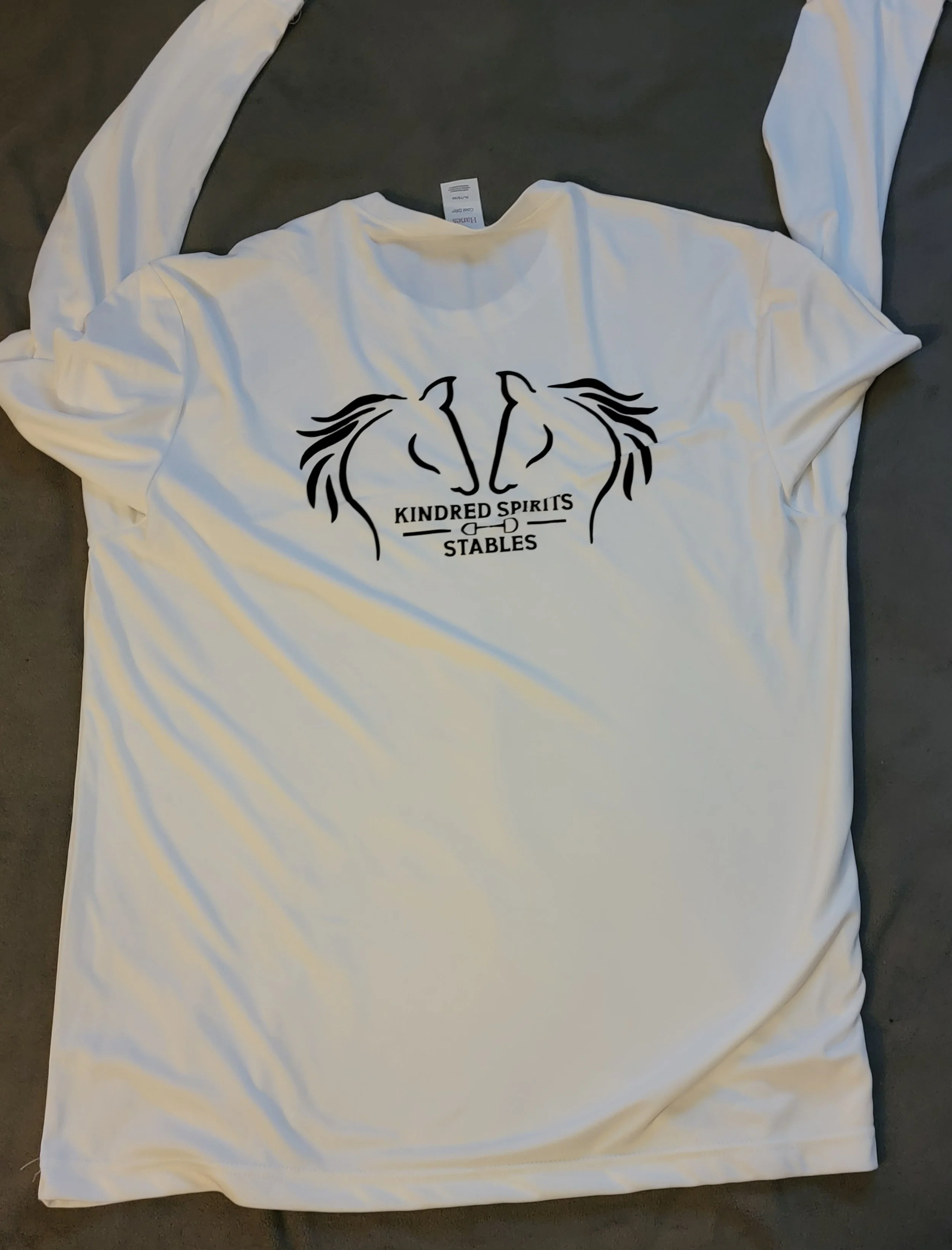 A white T-shirt with a black graphic of two horse heads facing each other and the text 'Kindred Spirits Stables' underneath.