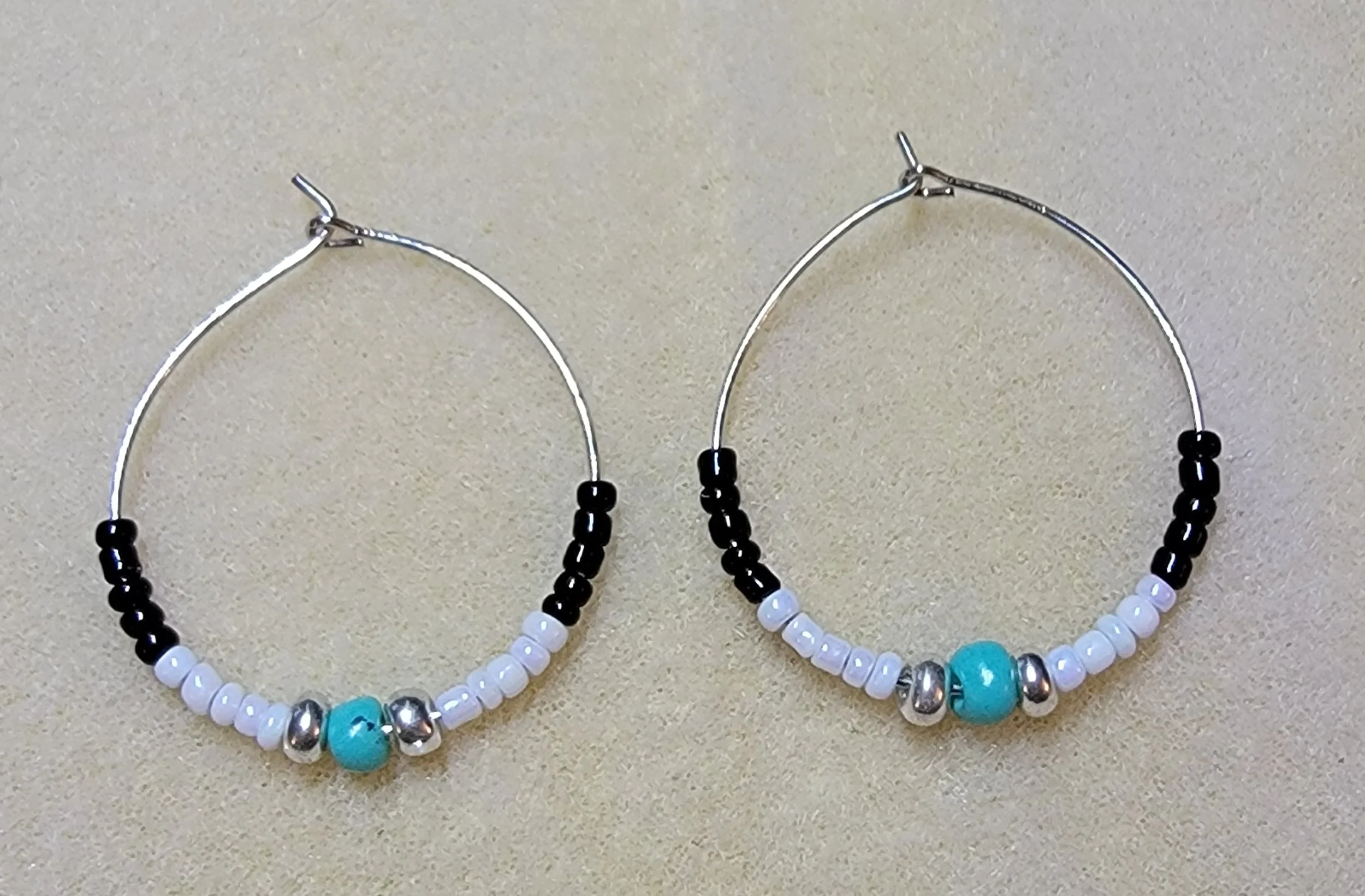 Pair of hoop earrings with beads: black, white, silver, and turquoise, on a neutral background.