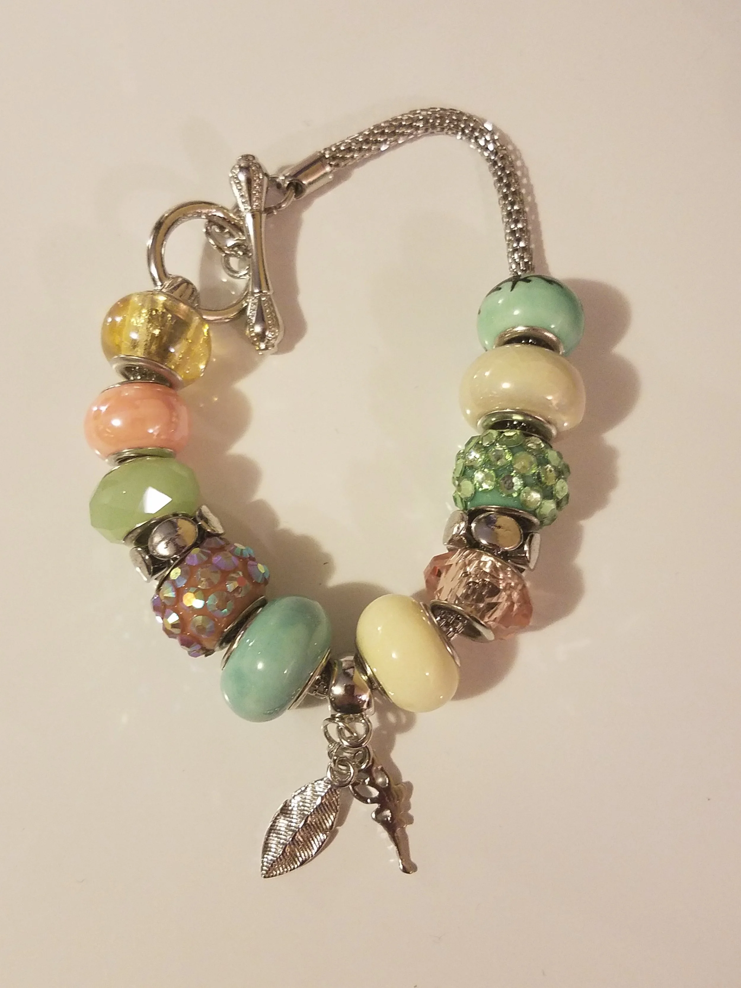 Colorful charm bracelet with various pastel-colored beads and charms, including a leaf and a person figure, on a light background.