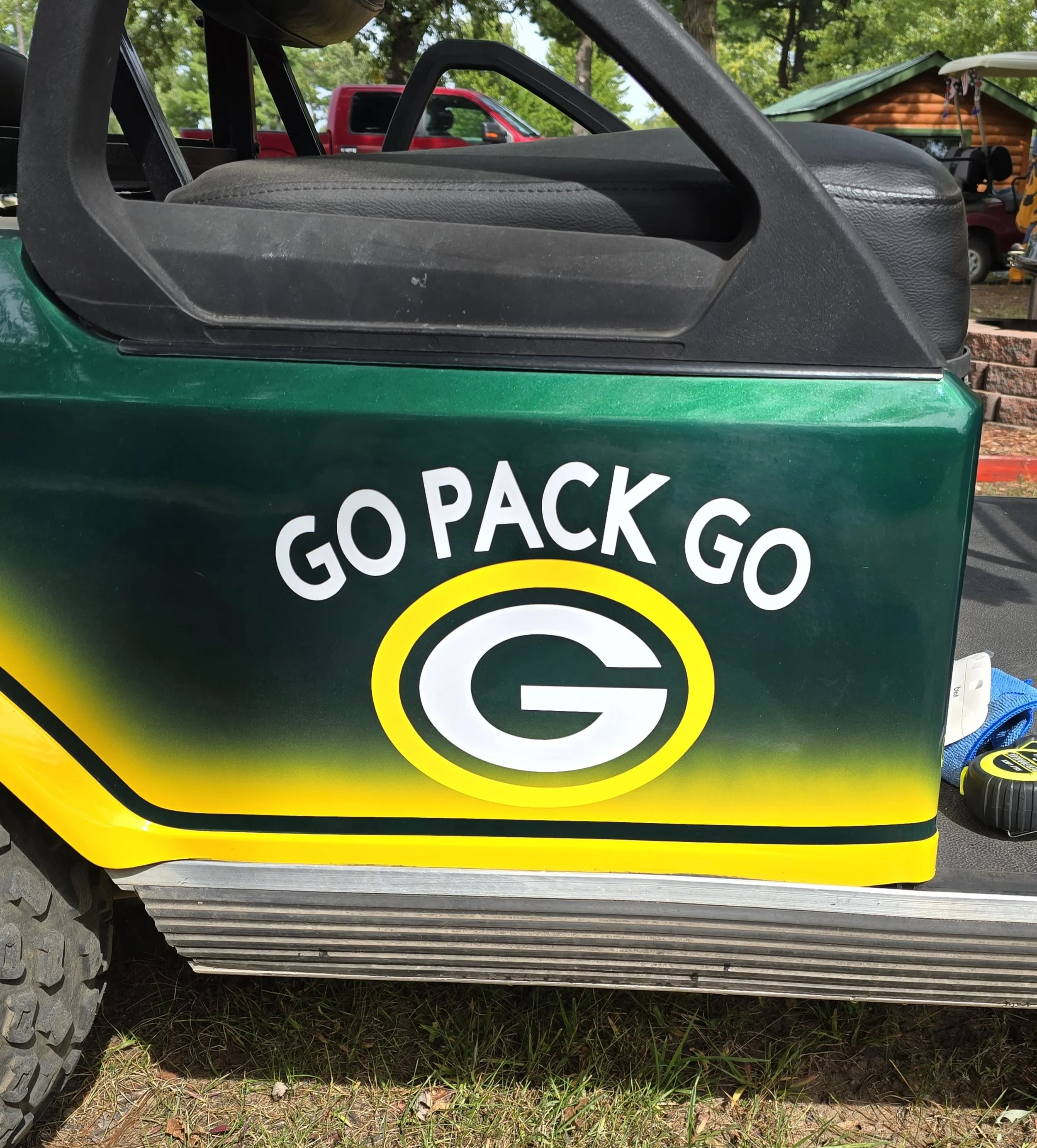 The side of a green golf cart with a decal featuring the Green Bay Packers logo and the slogan 'Go Pack Go' in white letters above the logo.