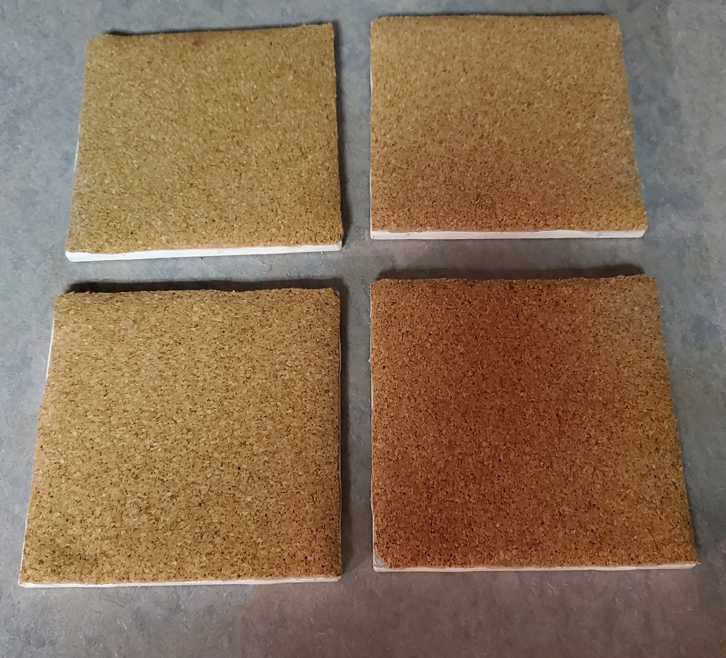 Four cork tiles arranged in a 2x2 grid on a gray surface, with two light brown tiles and two darker brown tiles.