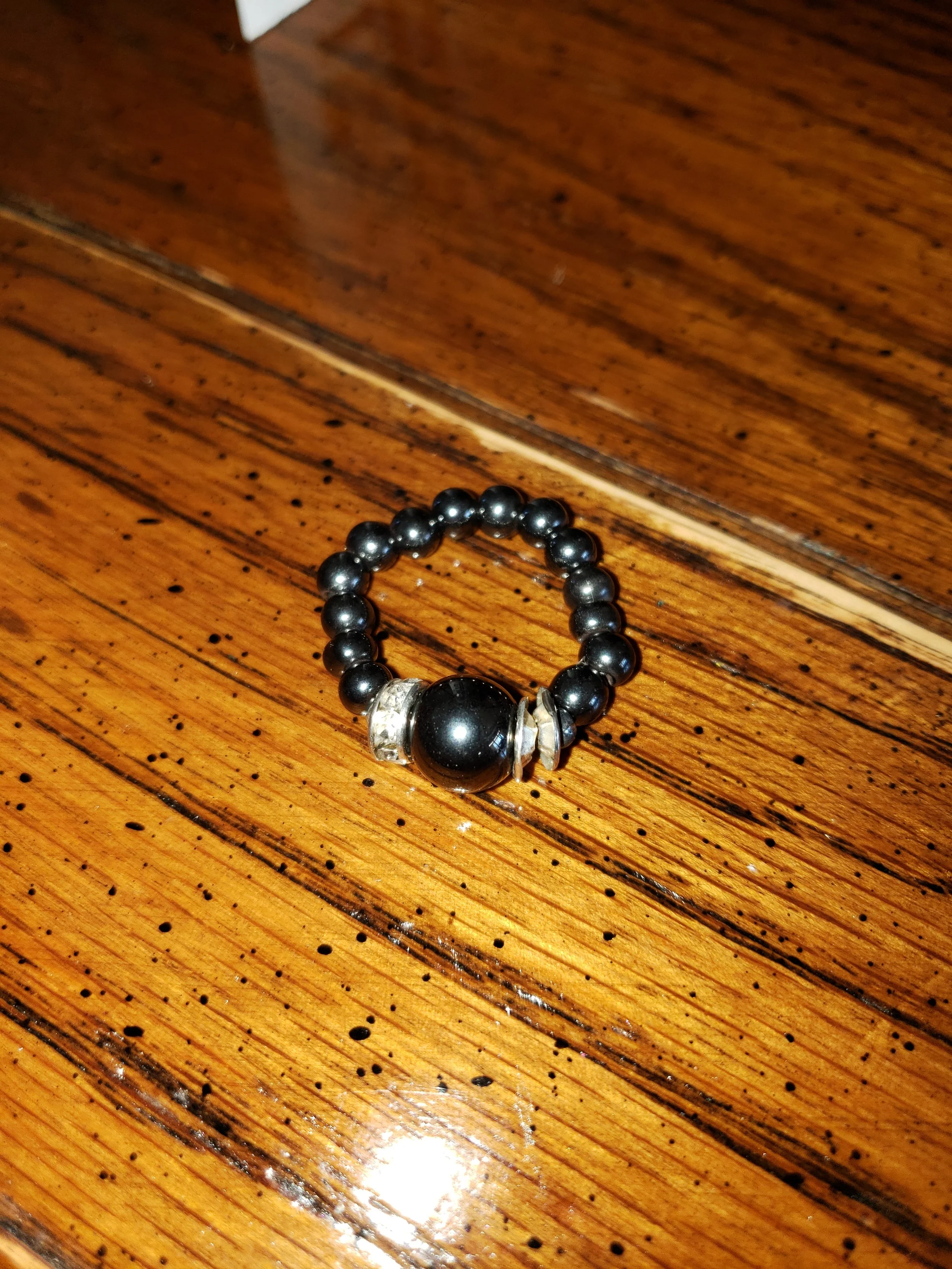 A ring made of black beads with a large black bead in the center, placed on a wooden surface.