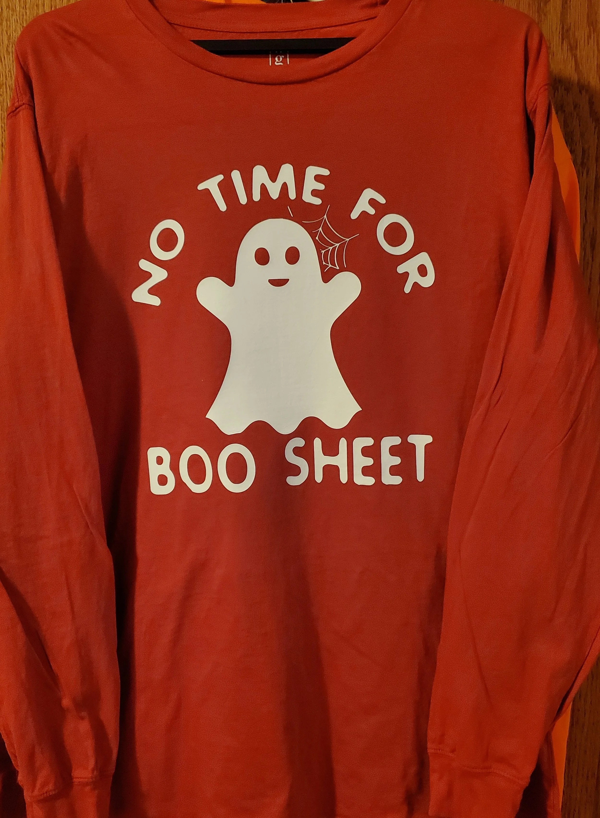 Orange long-sleeve shirt with a white ghost graphic and the phrase "No Time For Boo Sheet" in playful font, with a small web detail next to the ghost's head.