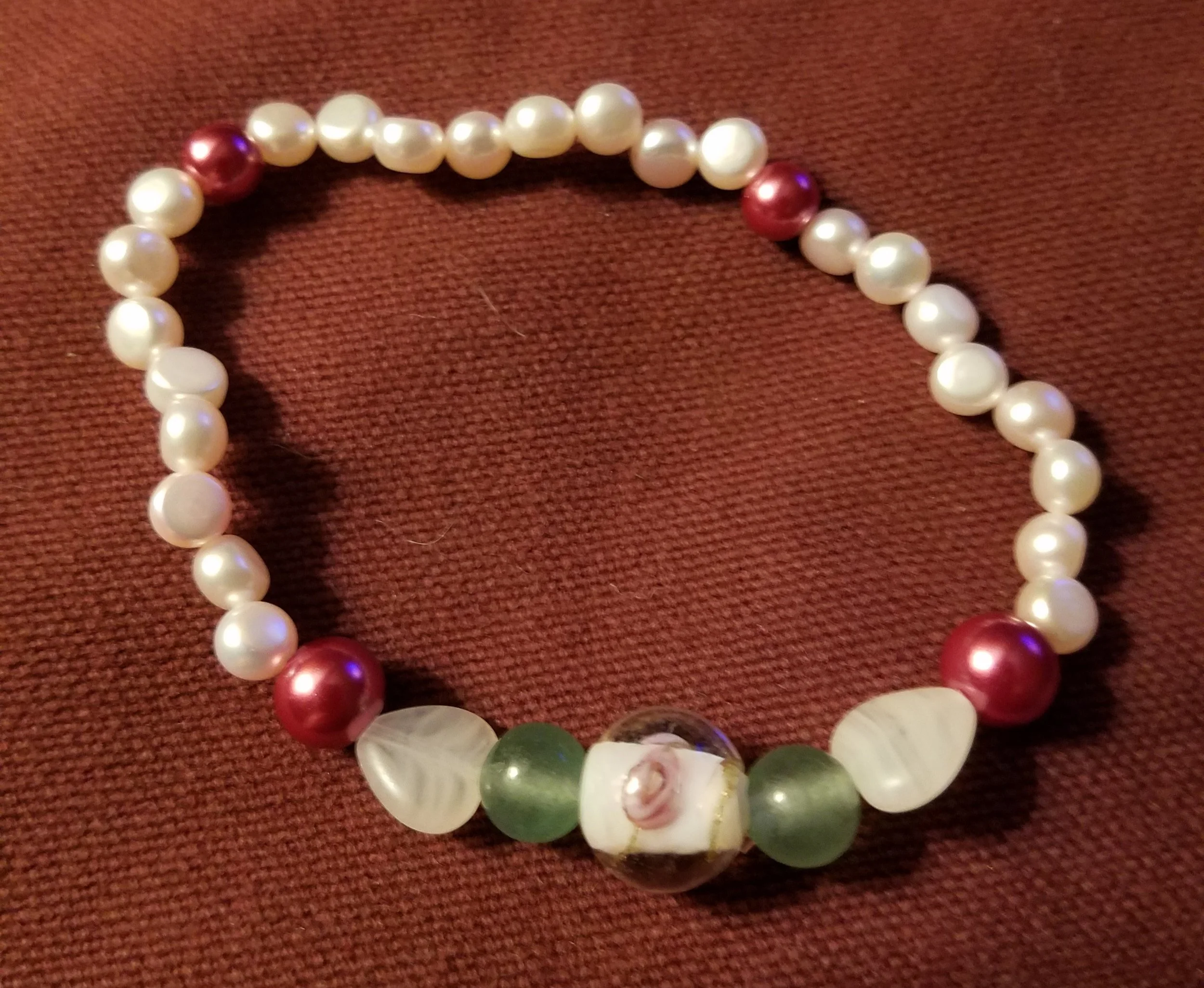 A necklace made of white pearls, red pearls, and other beads on a red fabric background.