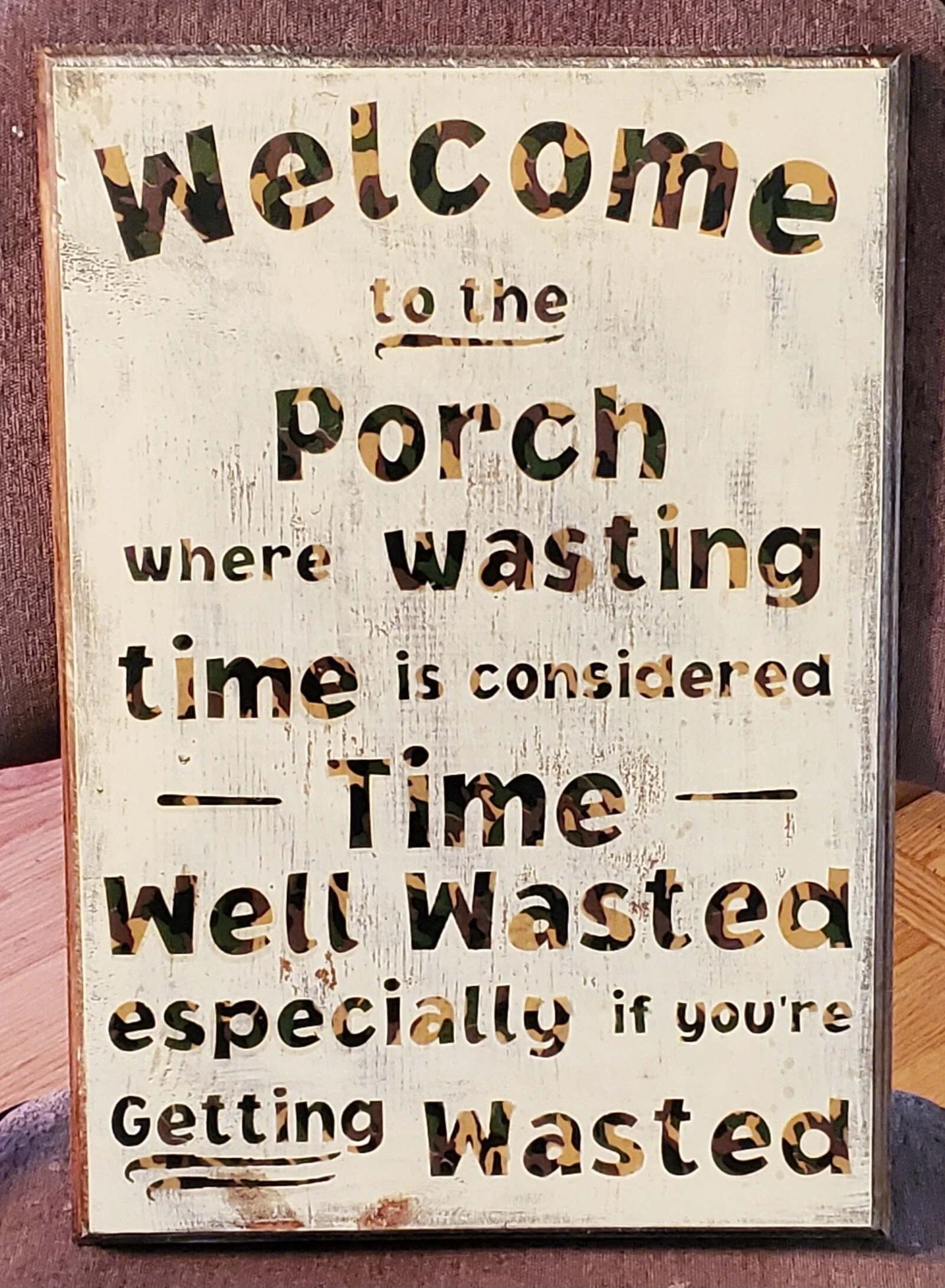 A decorative sign with cut-out letters spelling out a humorous message about watching television in the bathroom, with a distressed white wooden background and a wooden frame.