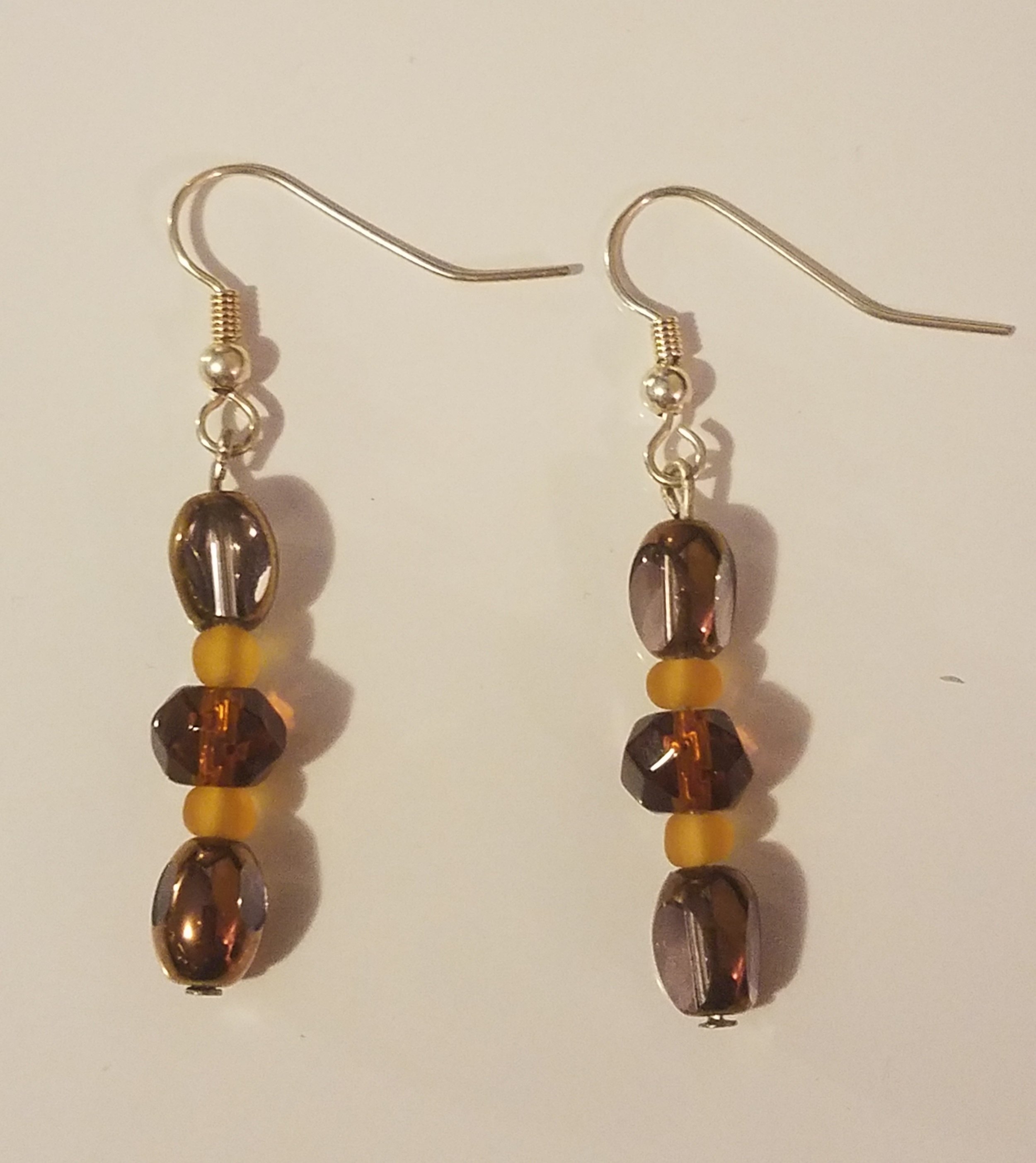 A pair of dangling earrings with beads in shades of brown and yellow, hanging from silver hooks.