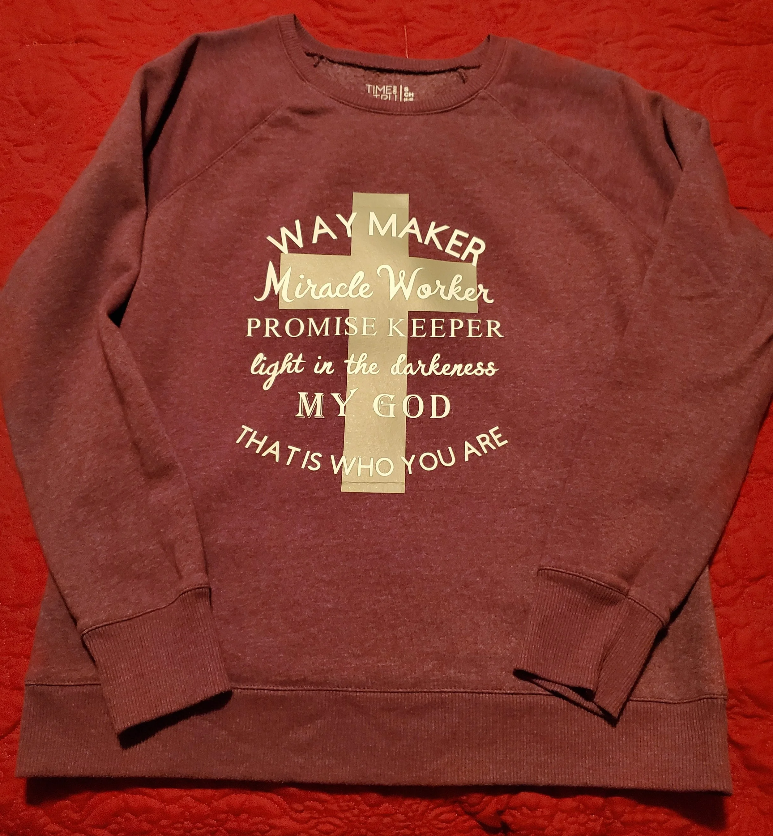 Maroon sweatshirt with Bible verse and cross graphic in beige and white text.