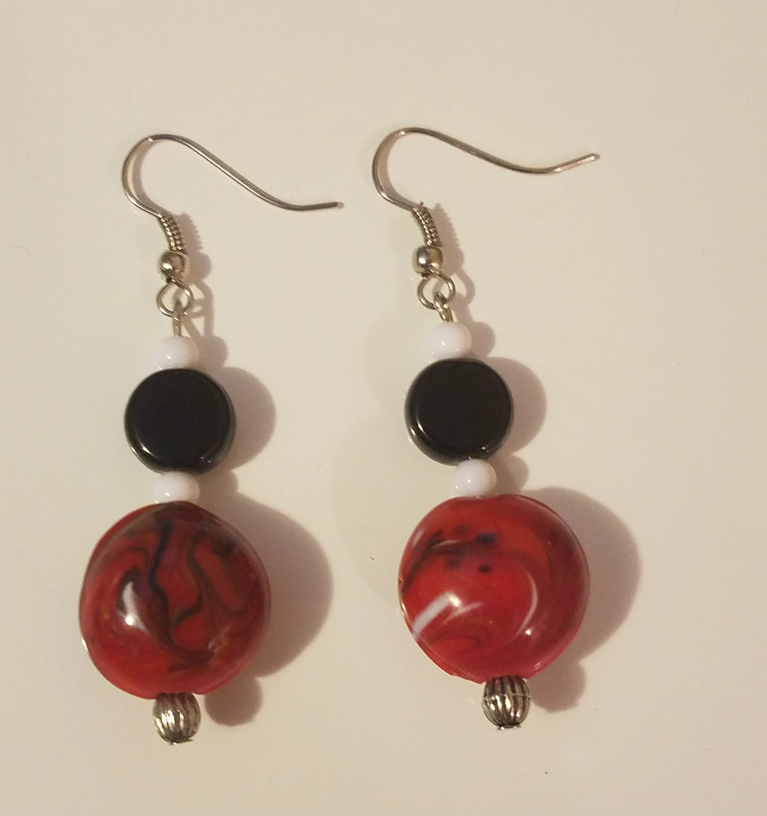 Pair of dangle earrings featuring black, white, and red marbled beads with silver accents, hanging from silver hooks.