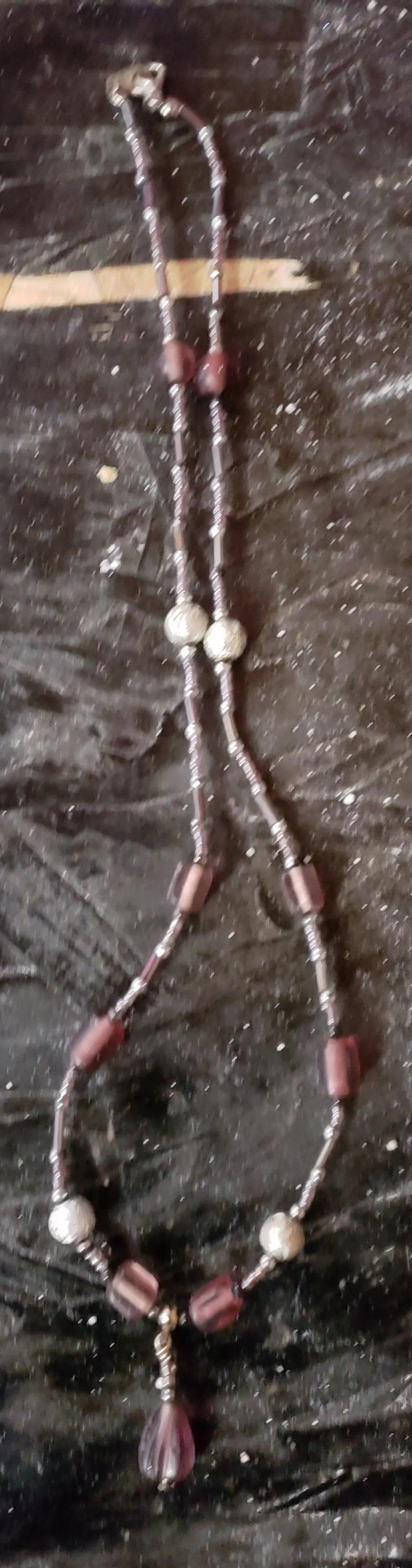 A necklace with beads and a pendant laid on a dark, textured surface.