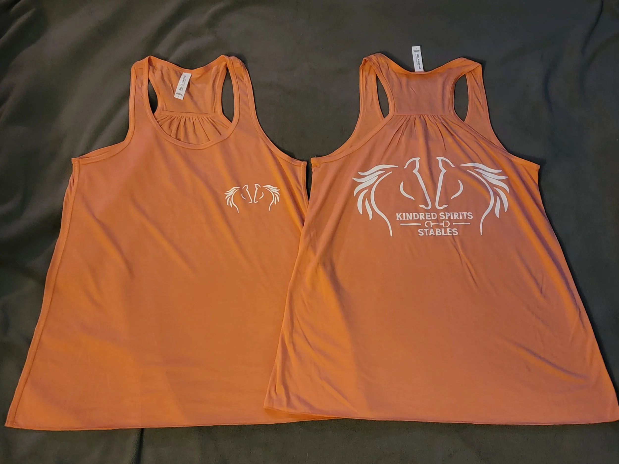 Two orange tank tops with white graphic designs on dark fabric background.
