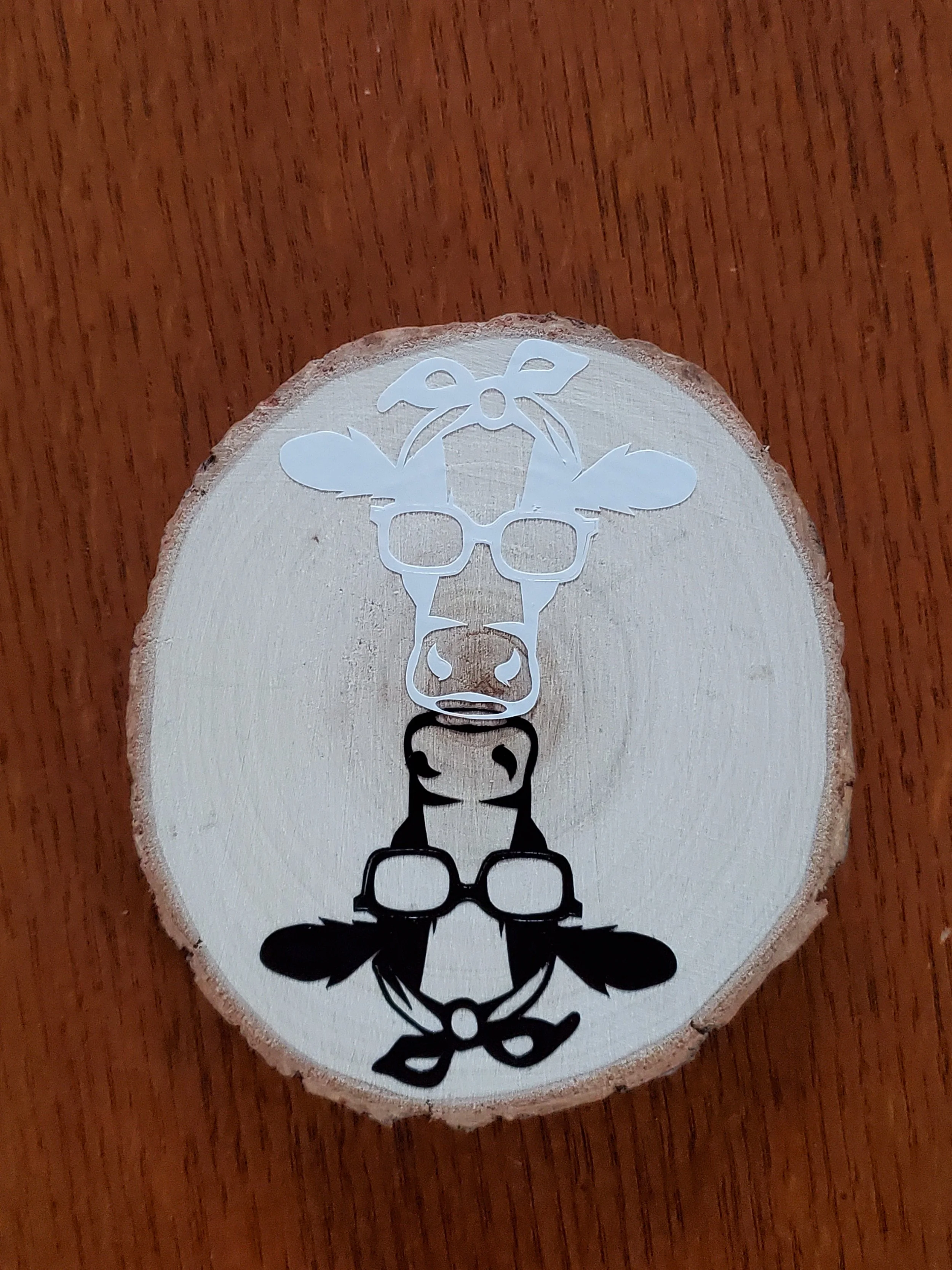 Decorative wooden piece with a design of a cow wearing glasses and a bow, with a floral bow on top, cut out of the wood.
