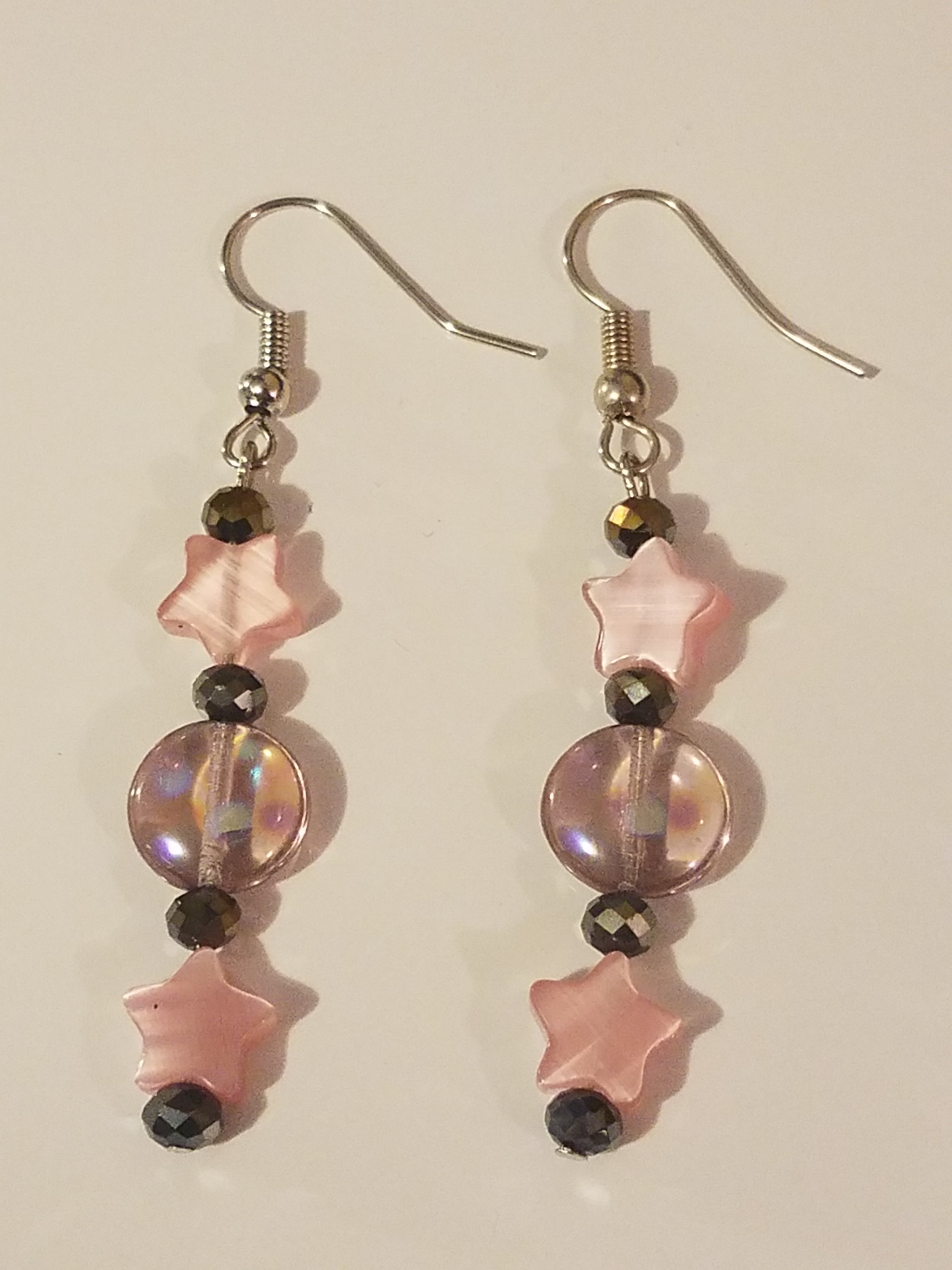 Earrings with pink star-shaped beads, black faceted beads, and clear round beads, on silver hooks.