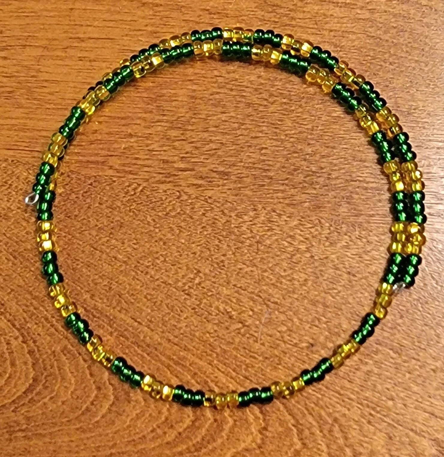 Green and yellow beaded necklace on wooden surface.