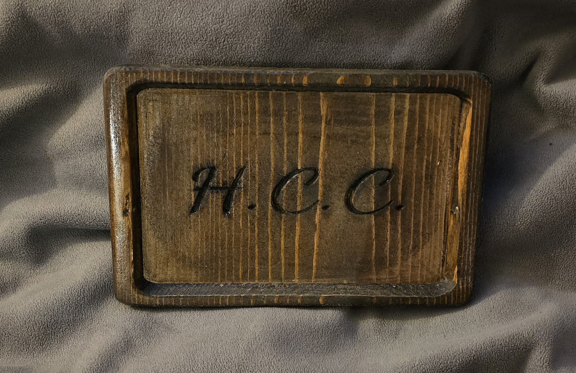 Wooden box with the initials H.C.C. engraved on top, placed on a gray fabric surface.