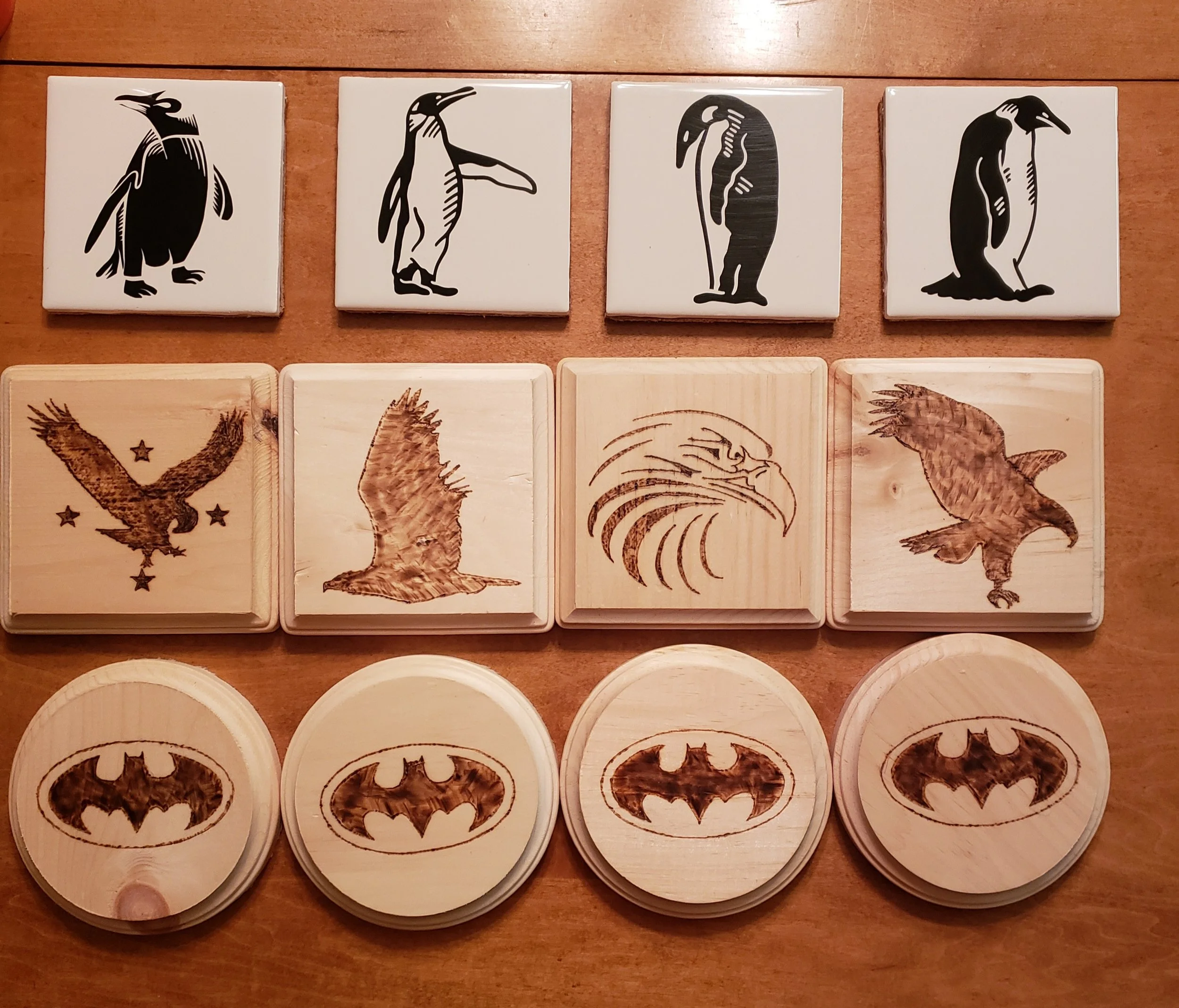 Various Batman-themed wooden and tile coasters with Batman logo and eagle illustrations, some featuring bird designs and stylized penguins.