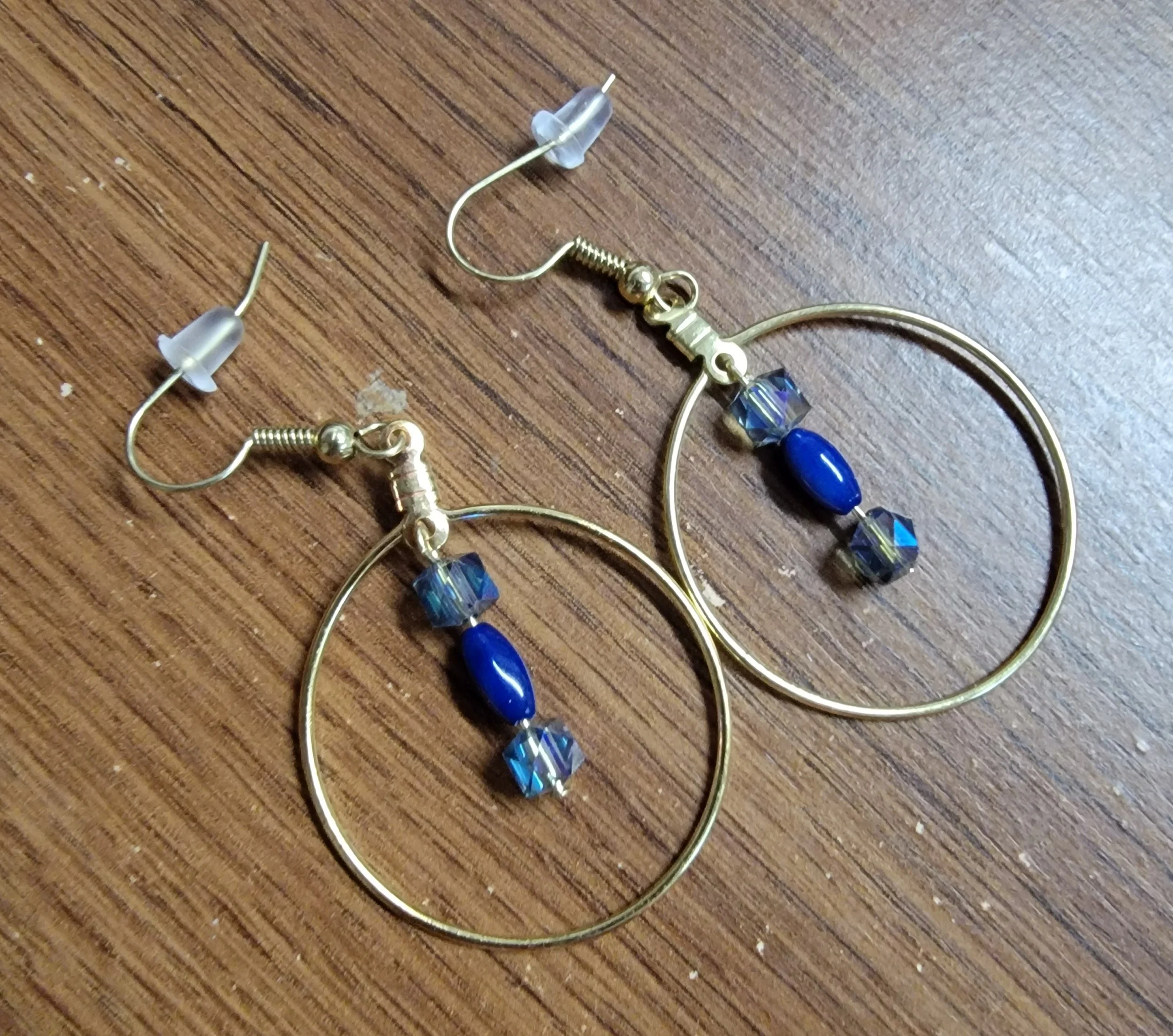 A pair of gold hoop earrings with blue and clear beads displayed on a wooden surface.
