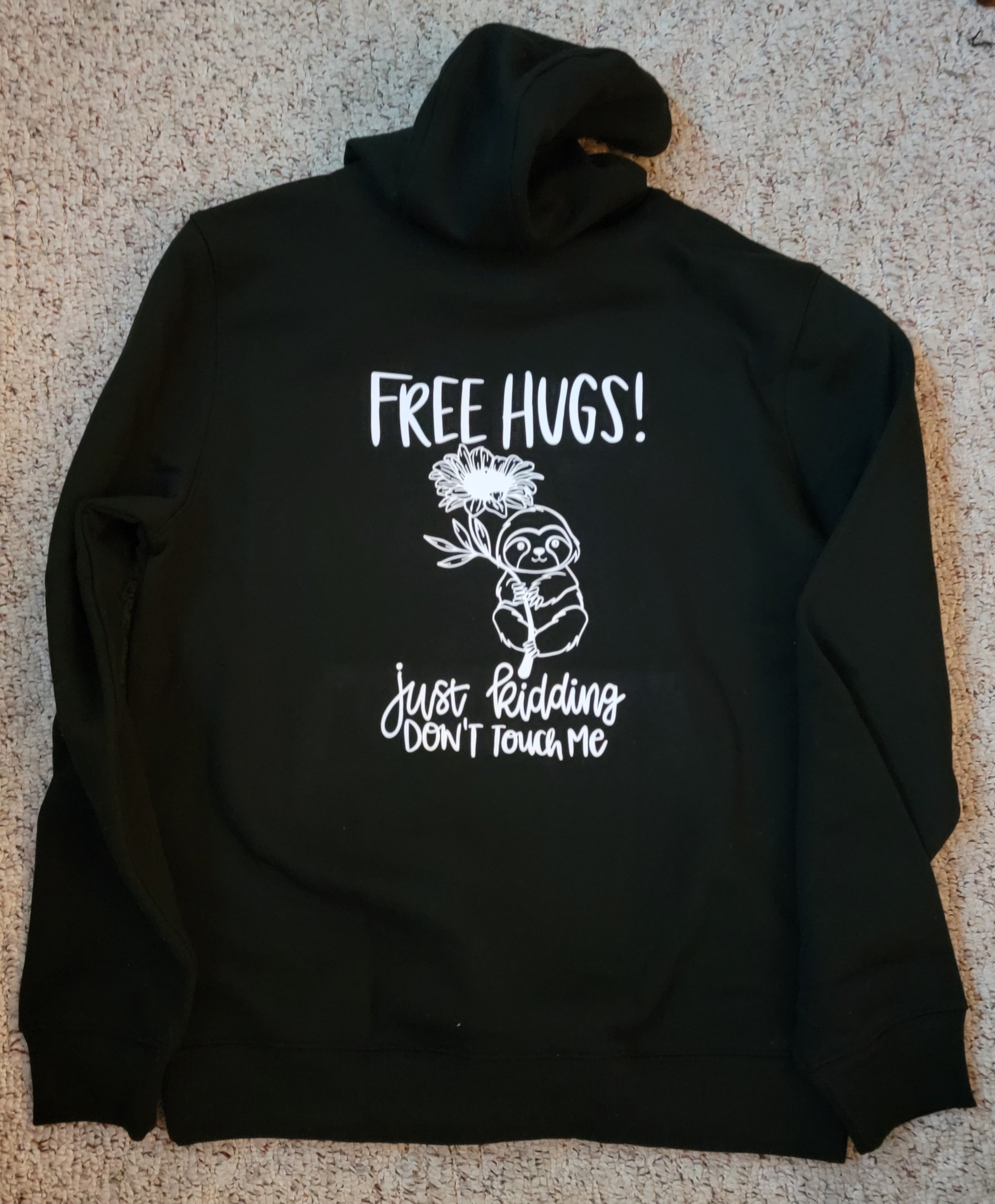 Black hoodie with a graphic of a cute sloth holding a flower and text that says, 'Free Hugs! Just Riding Don't Touch Me'.