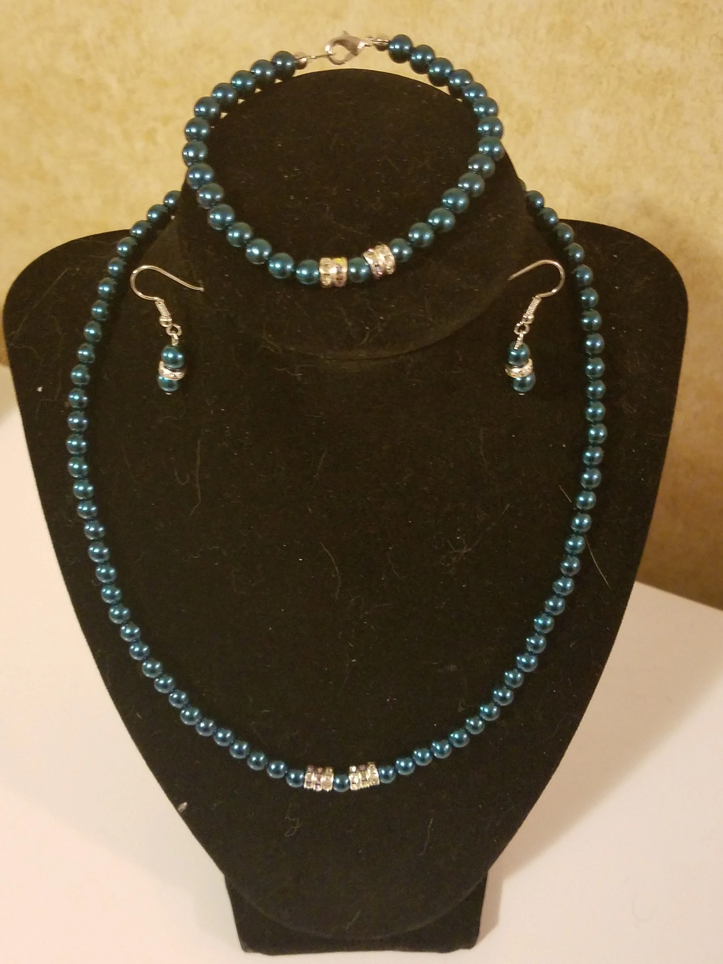 Blue bead jewelry set including a necklace, earrings, and bracelet, displayed on a black jewelry stand.