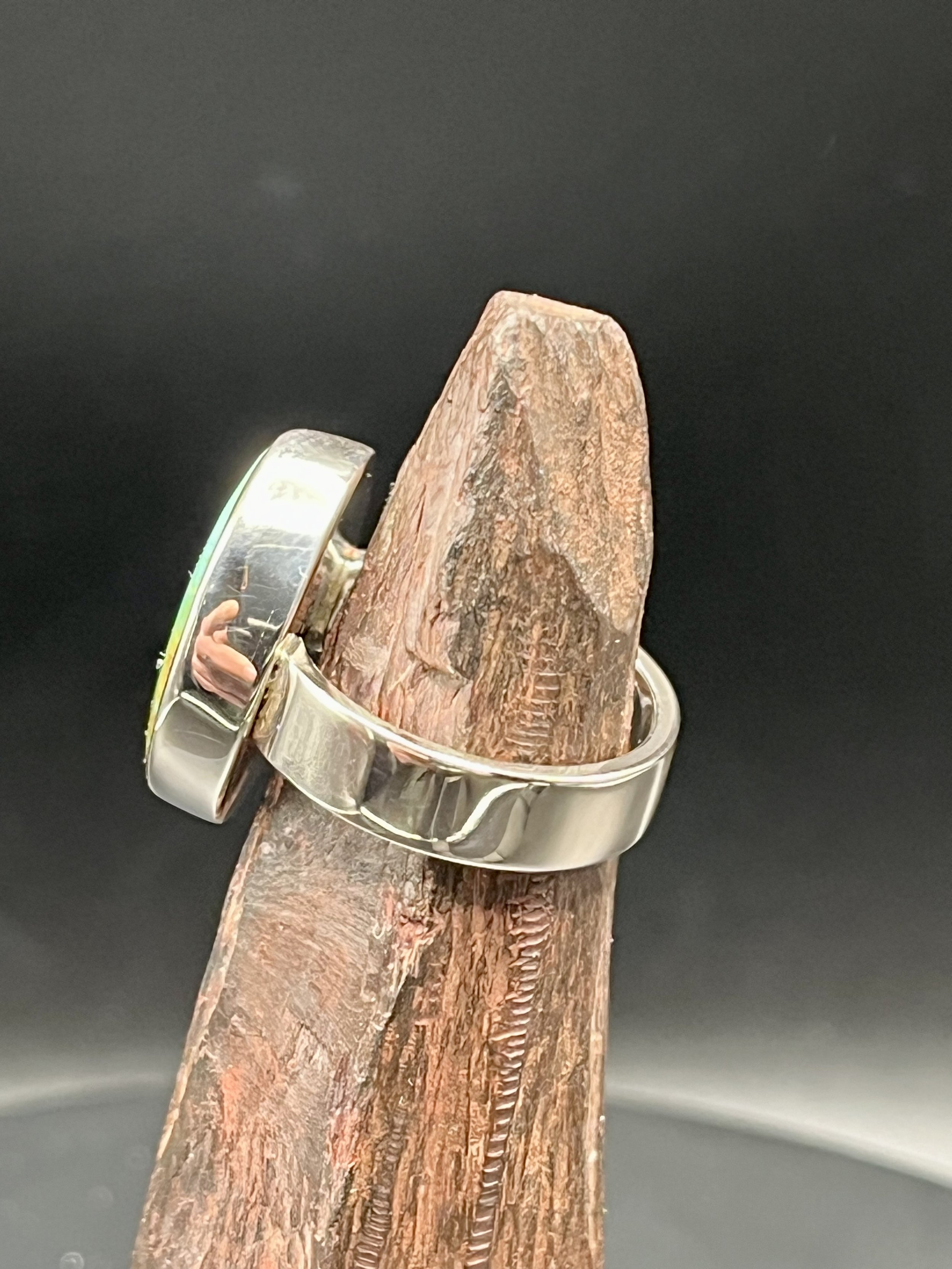 KC Silversmith's Kingman turquoise silver ring displayed on a jagged, rust-colored rock. The ring is angled 90 degrees away from the camera to showcase the silver band.