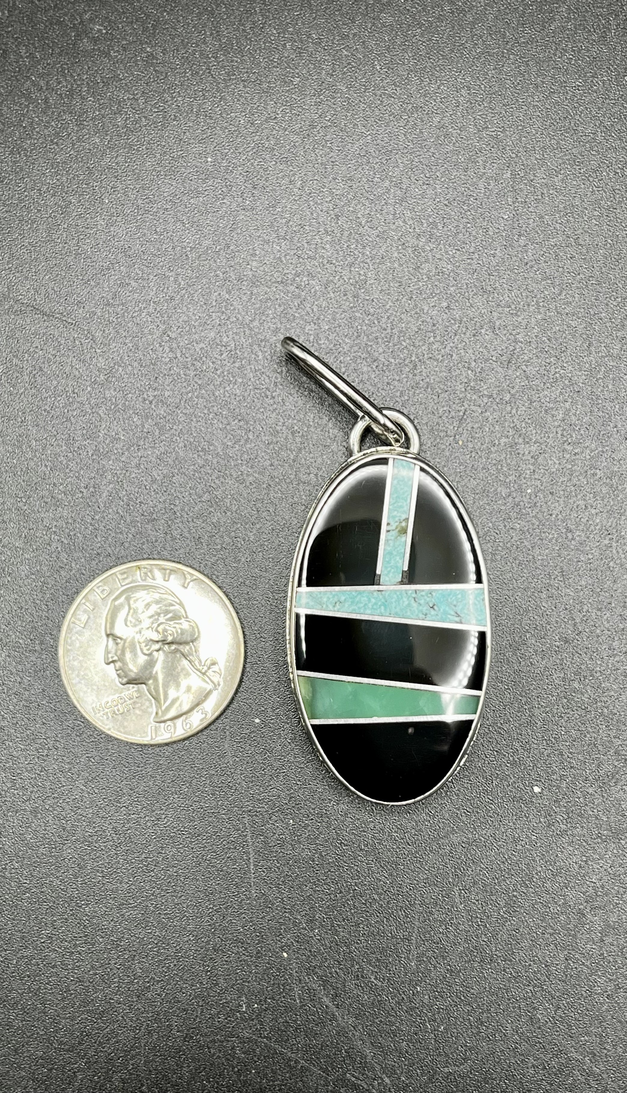 A blue and black inlay pendant on a black backdrop next to a quarter.