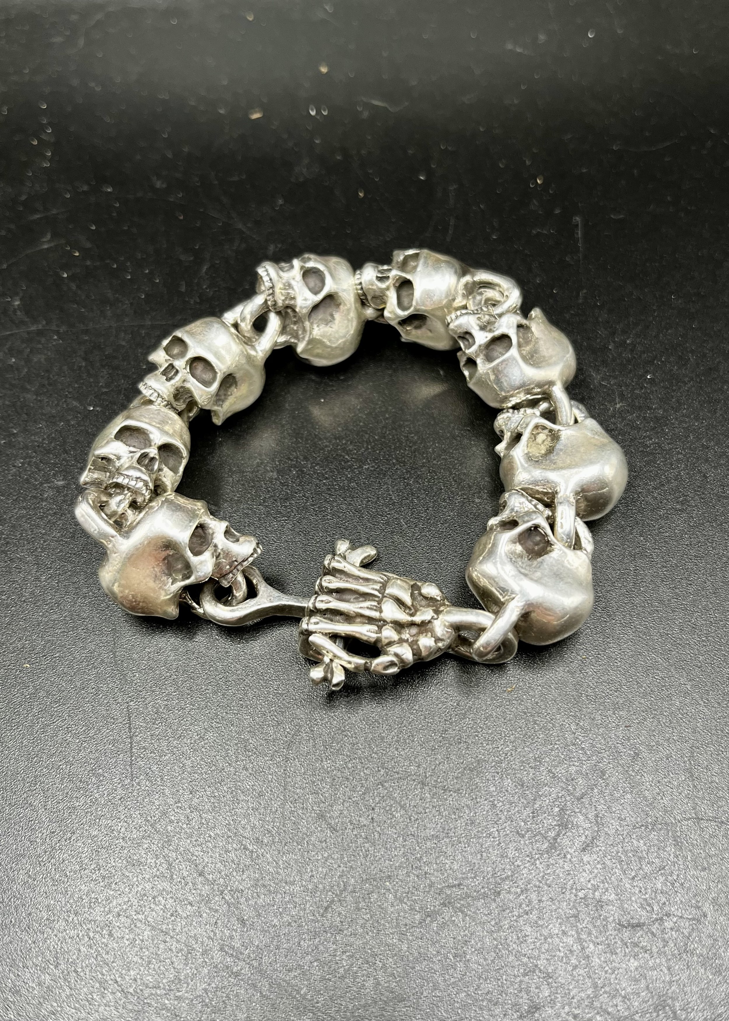 A bracelet of several hand-crafted skulls laid out on a black backdrop, linked together in a circle.