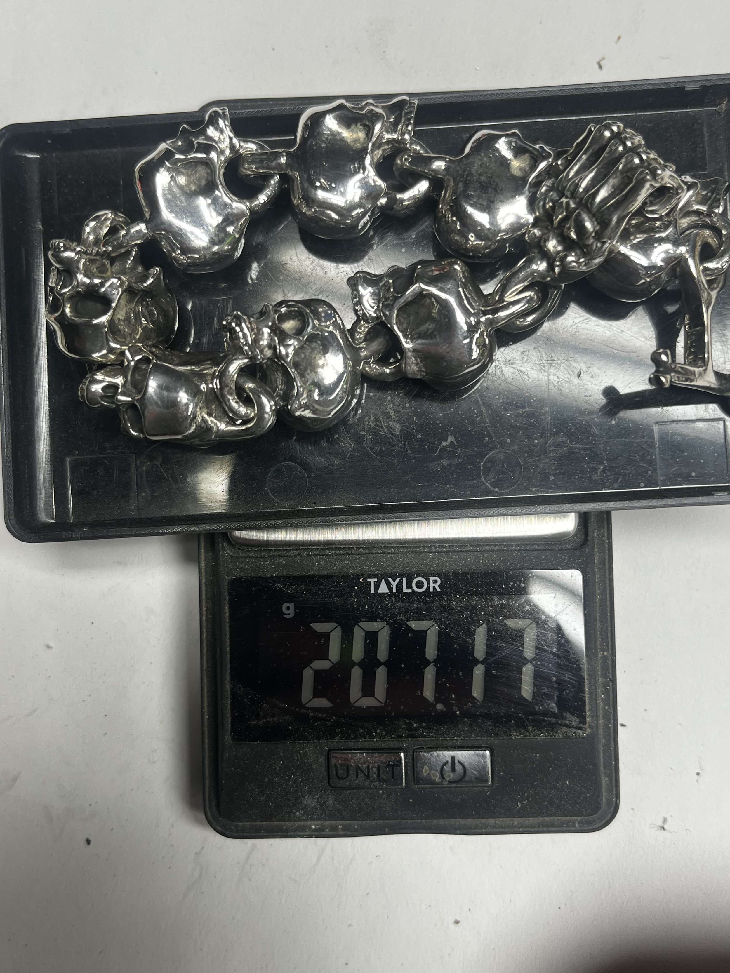 The components of KC Silversmith's sterling silver skull link bracelet laid out on a scale.
