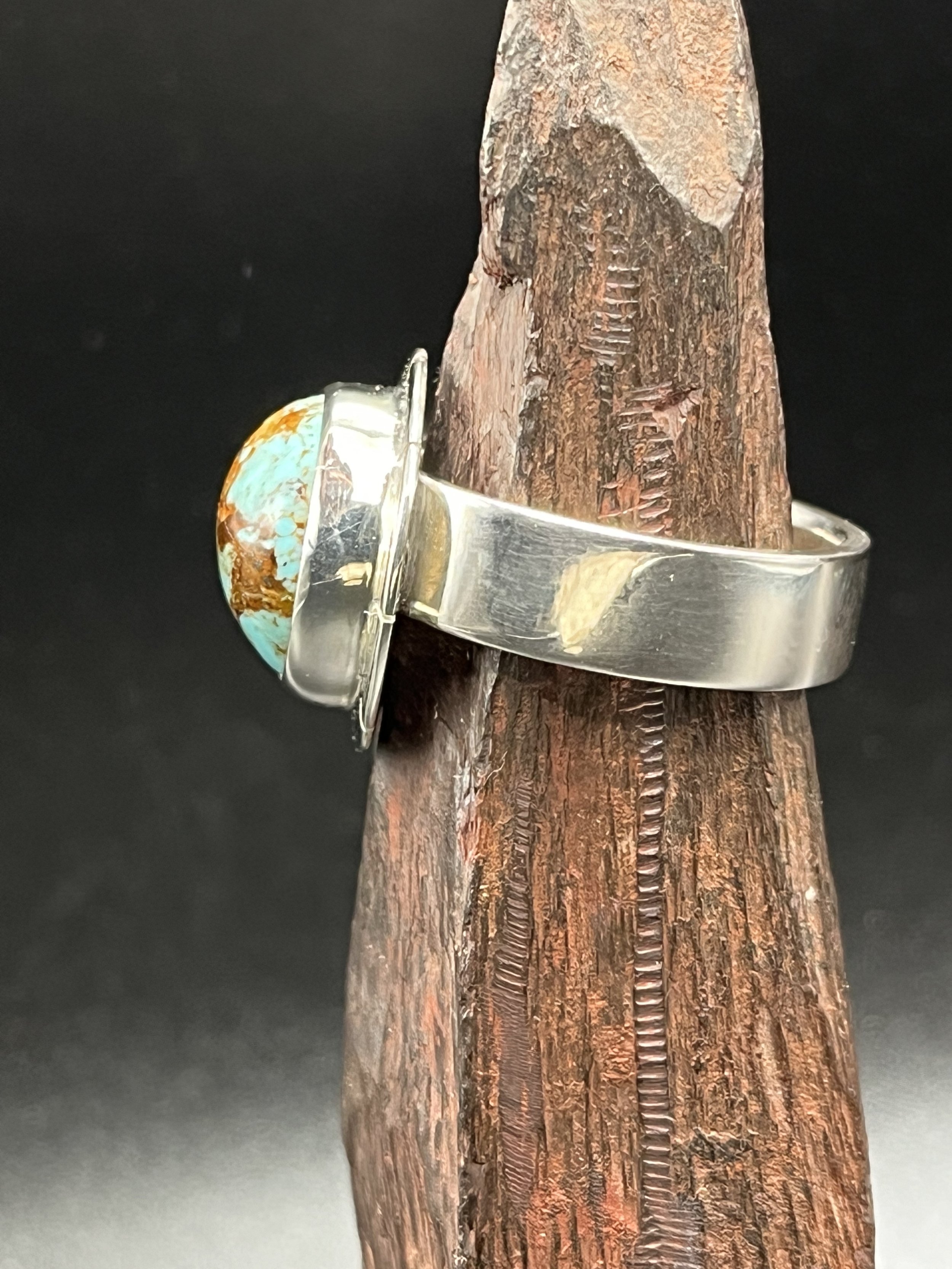 A ring custom-designed by KC Silversmith featuring a turquoise nugget, displayed on a dagged, rust-colored rock. The ring is angled away from the camera to showcase the sterling silver band.