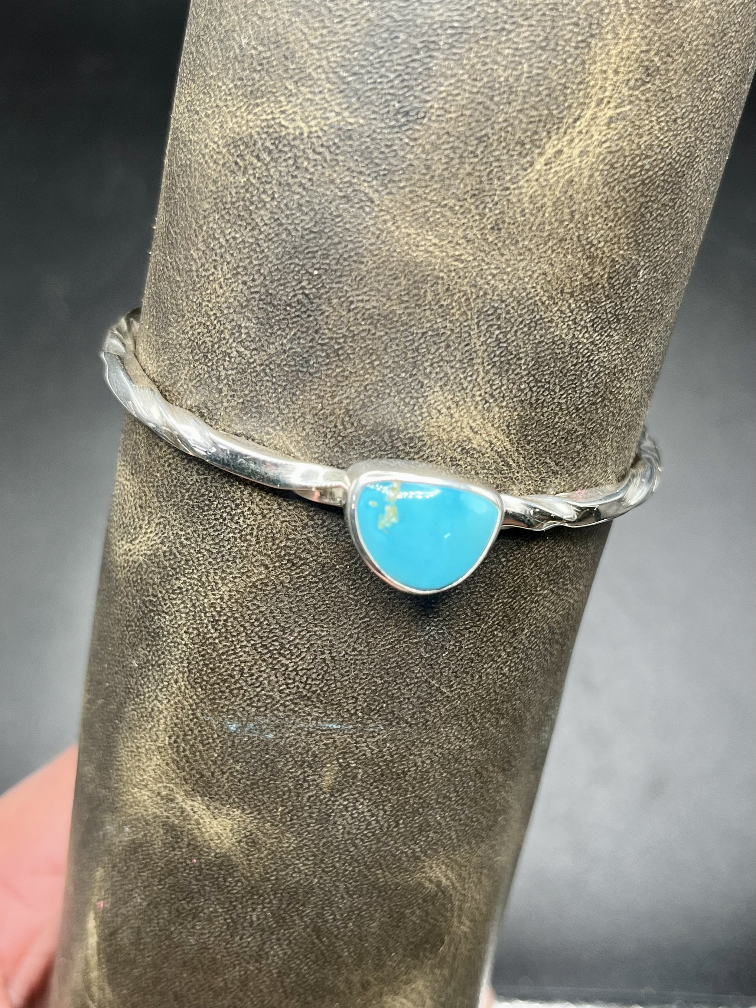 A bracelet with a twisted metal band and large turquoise gemstone displayed on a mannequin's arm.