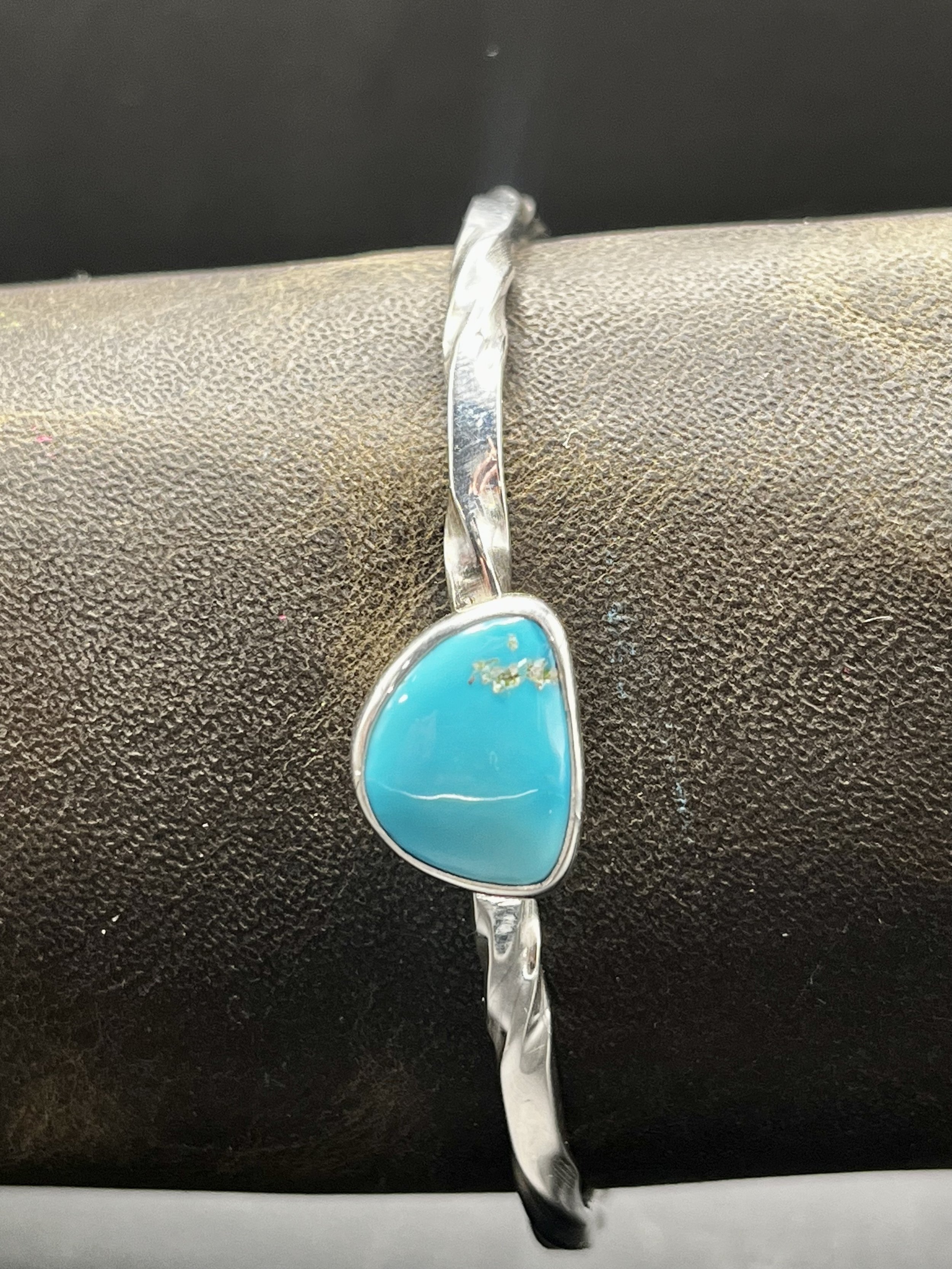 A bracelet with a twisted metal band and large turquoise gemstone displayed on a mannequin's arm.