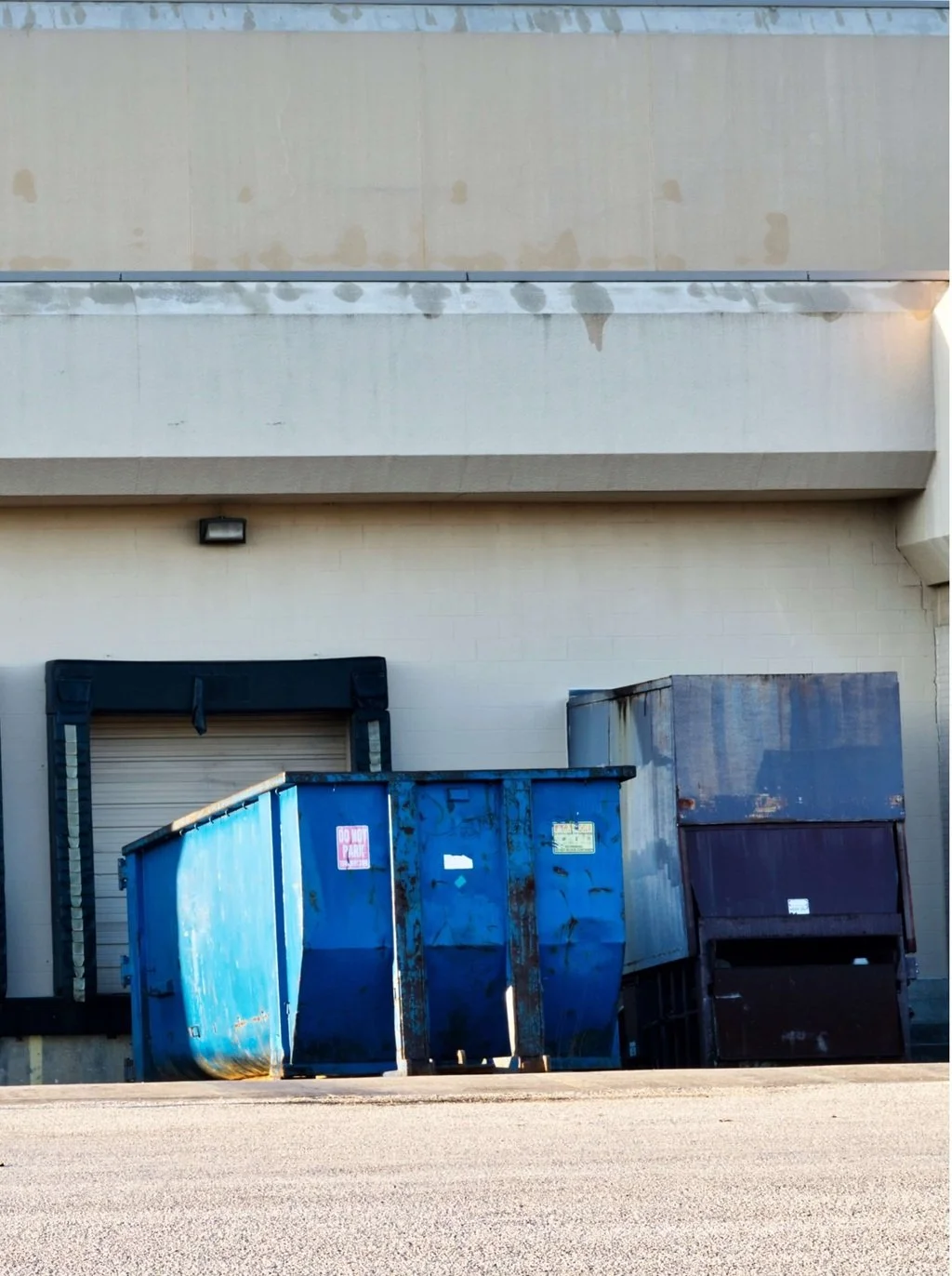 Commercial building with a blue dumpster and recycling bin