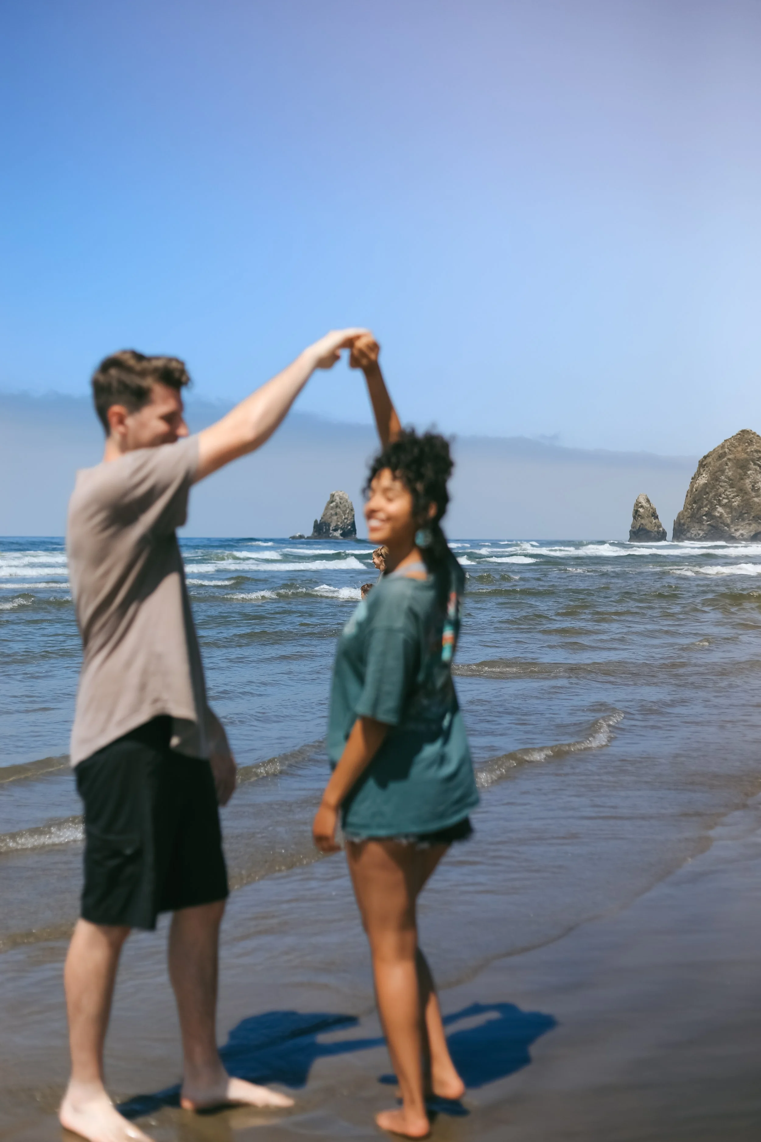 A couple dancing on a beach with rocks visible in the ocean.