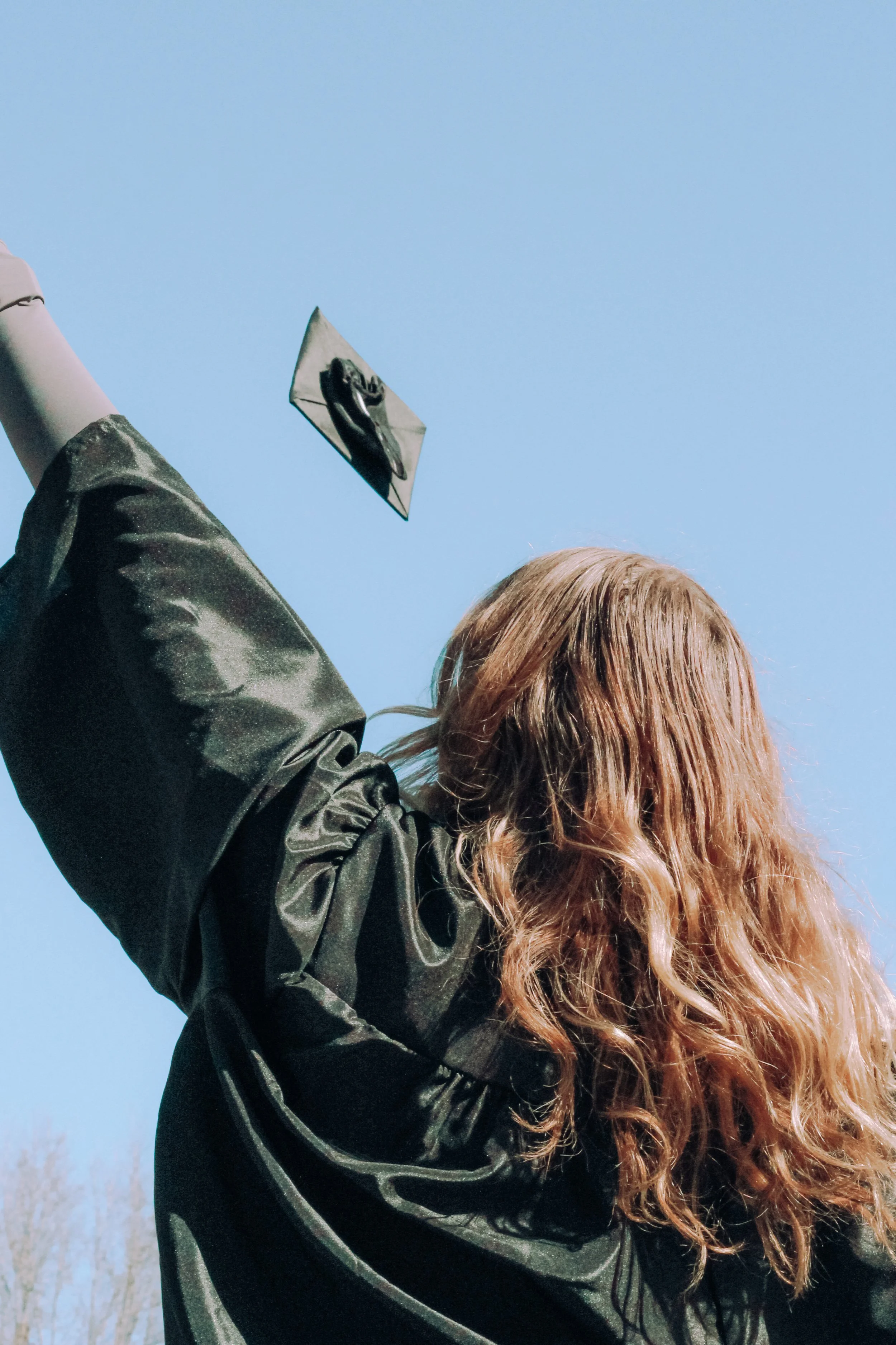 Graduate raising arm, cap in sky, blue background.