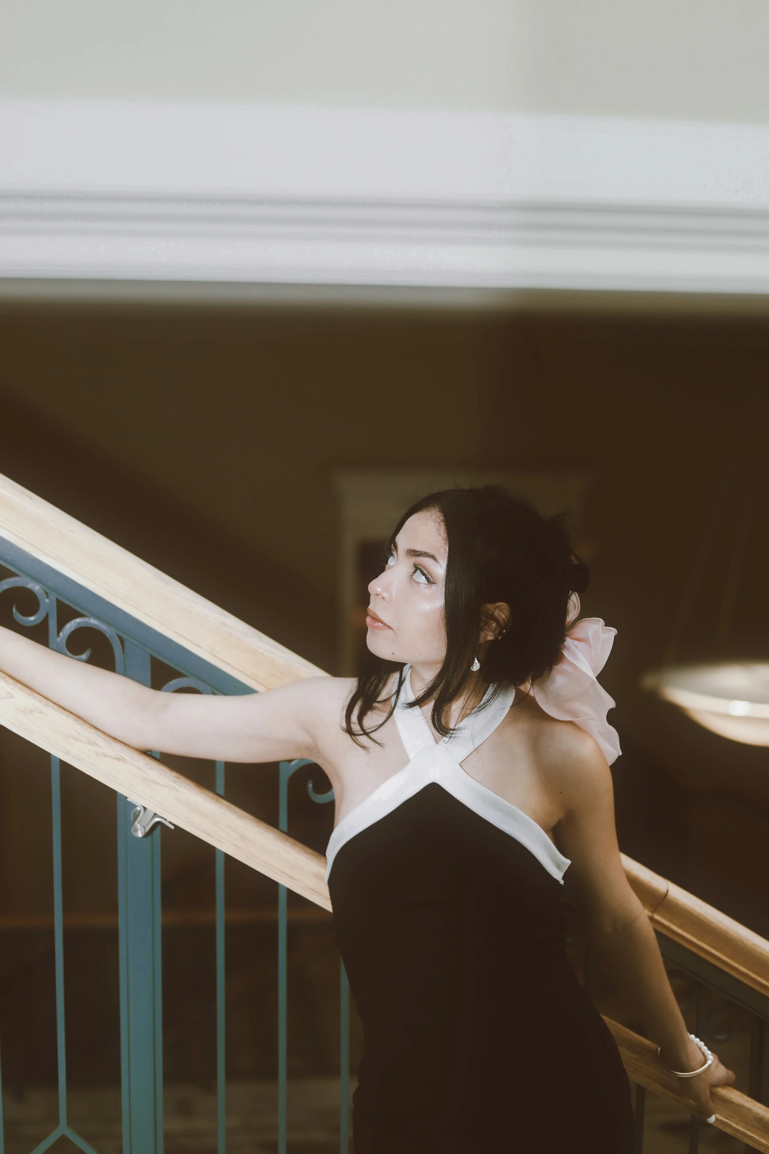 Woman in black and white dress standing on staircase indoors, looking up.