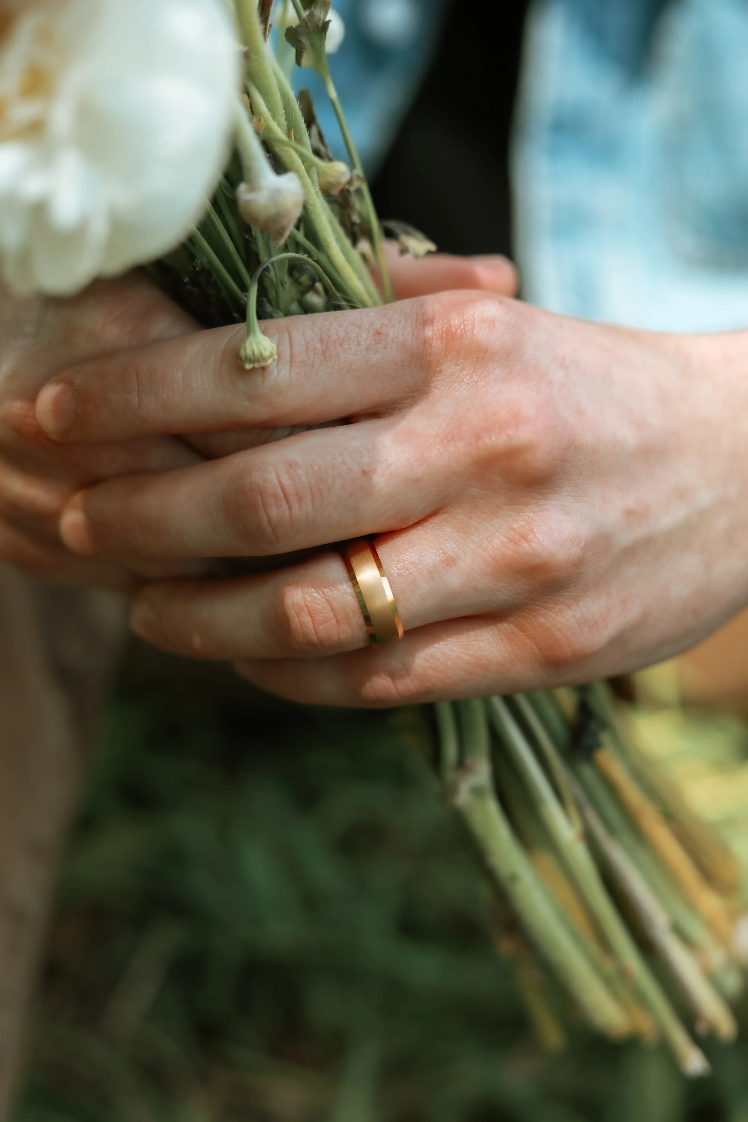 Hands holding a bouquet of flowers, wearing a gold ring