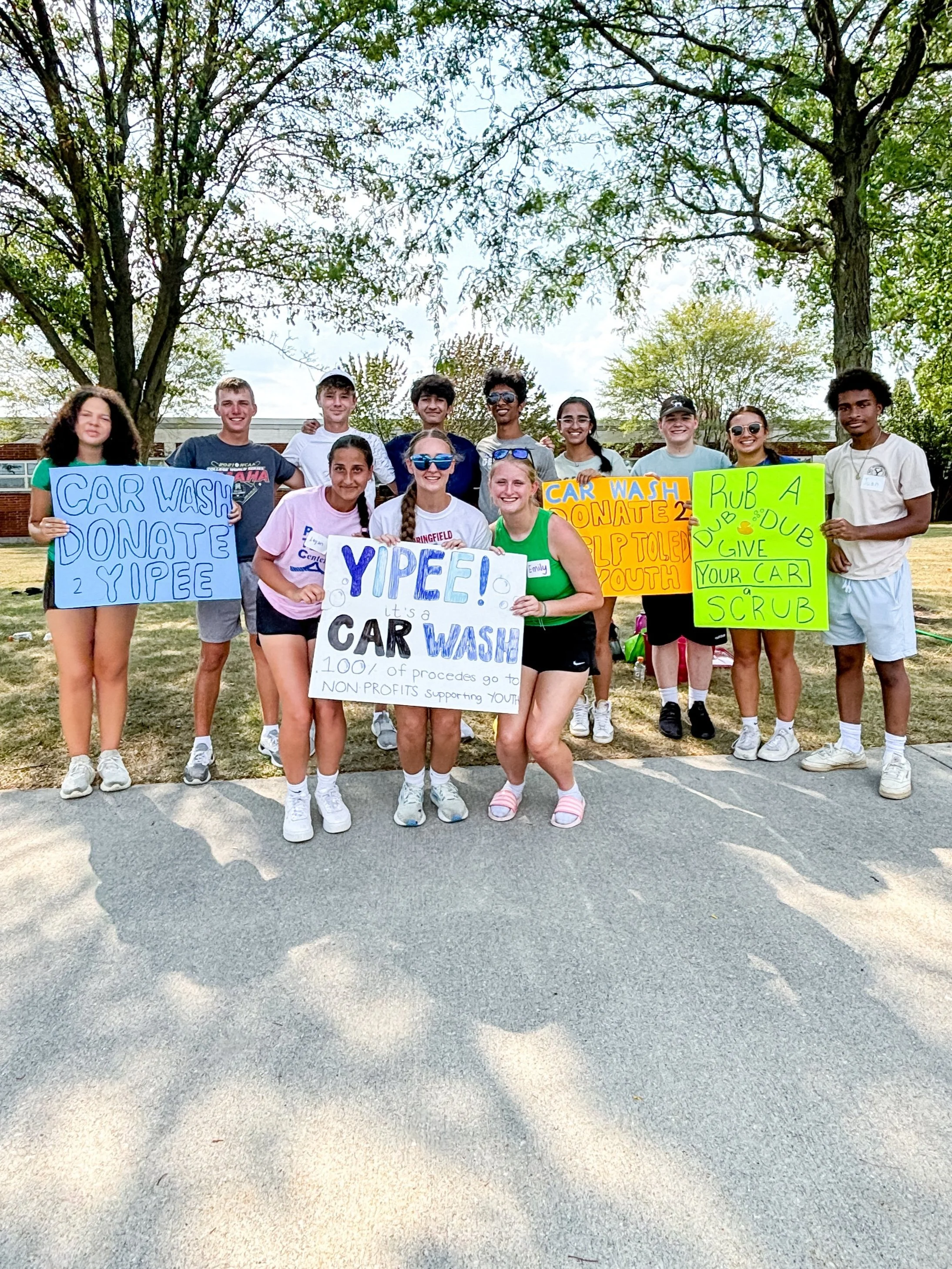 YIPEE members stand together, smiling and holding signs advertising a car wash