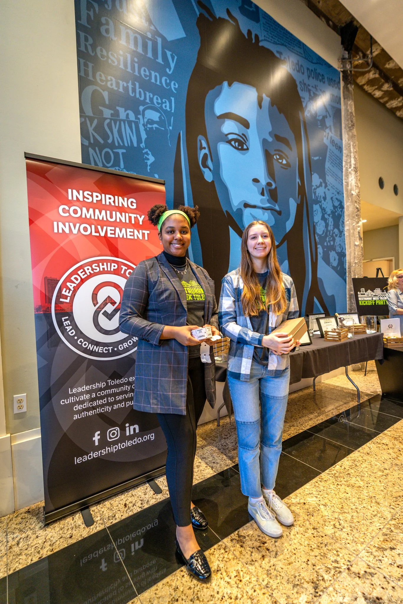 Two YIPEE students stand in front of a Leadership Toledo Banner while selling raffle tickets