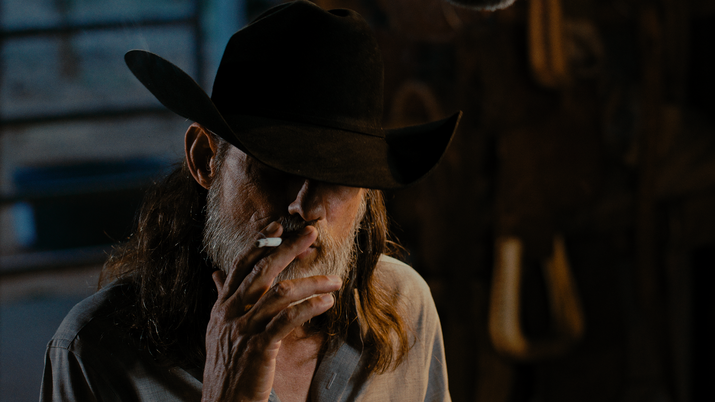 Weathered cowboy in a black hat smoking a cigarette in dim light