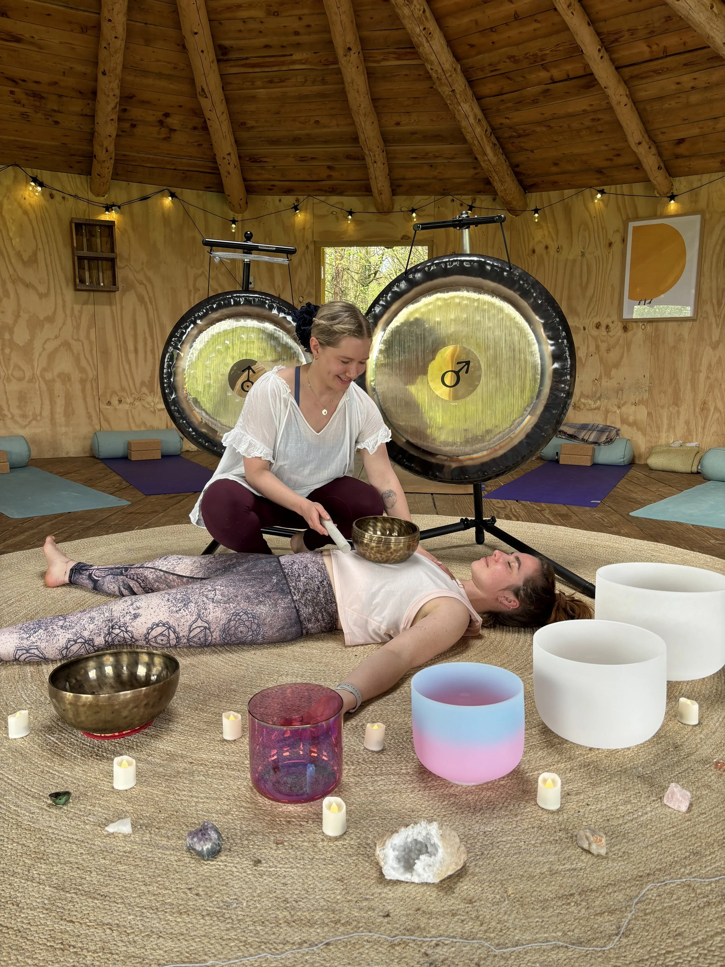 two women, one performing sound healing with a tibetan bowl on the other who is lying down