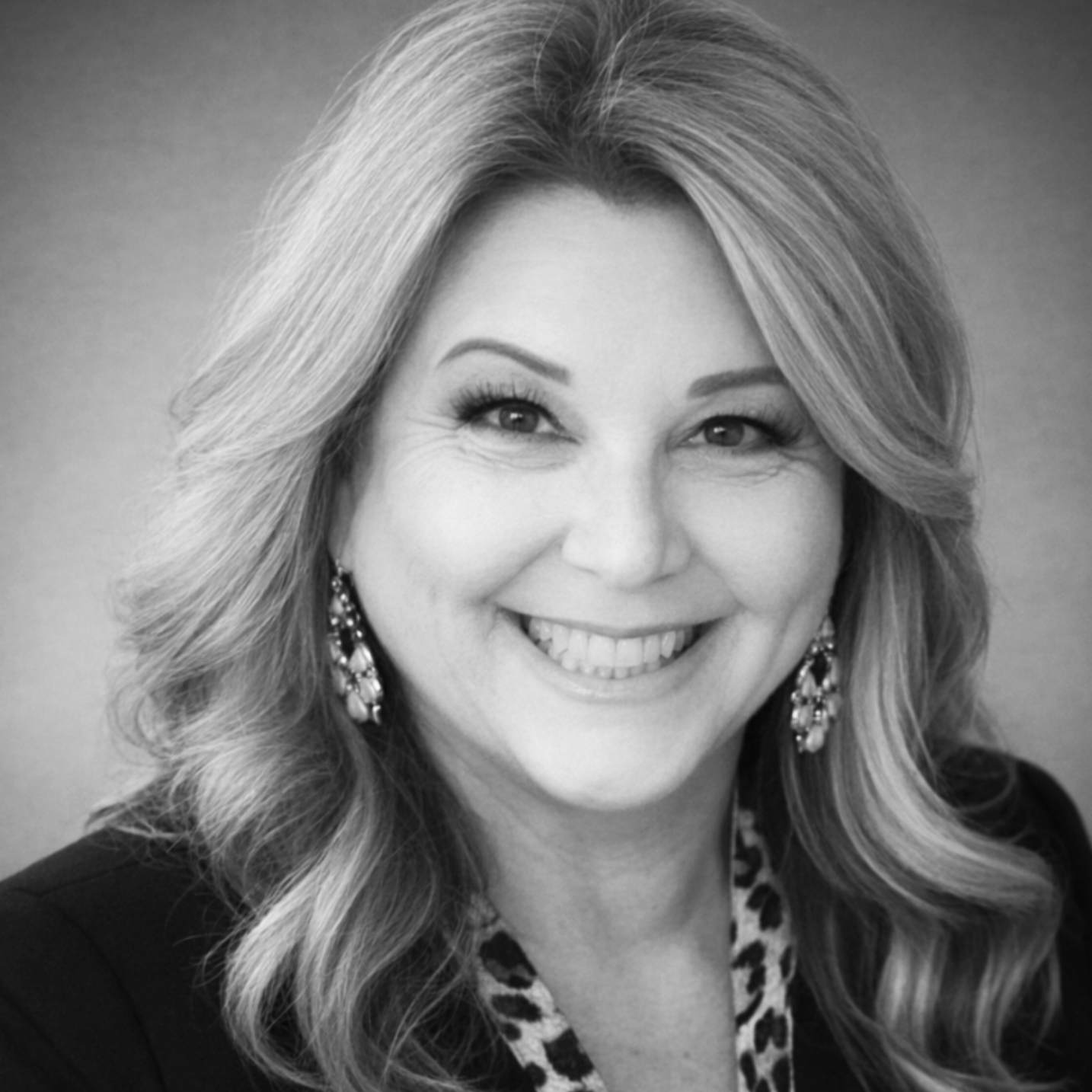 Black and white headshot of a Jenn Morris who is former principal in Upland, California, and now a content and engagement expert with Peopling. Sh has long, wavy hair, smiling, wearing earrings and a leopard print blouse.