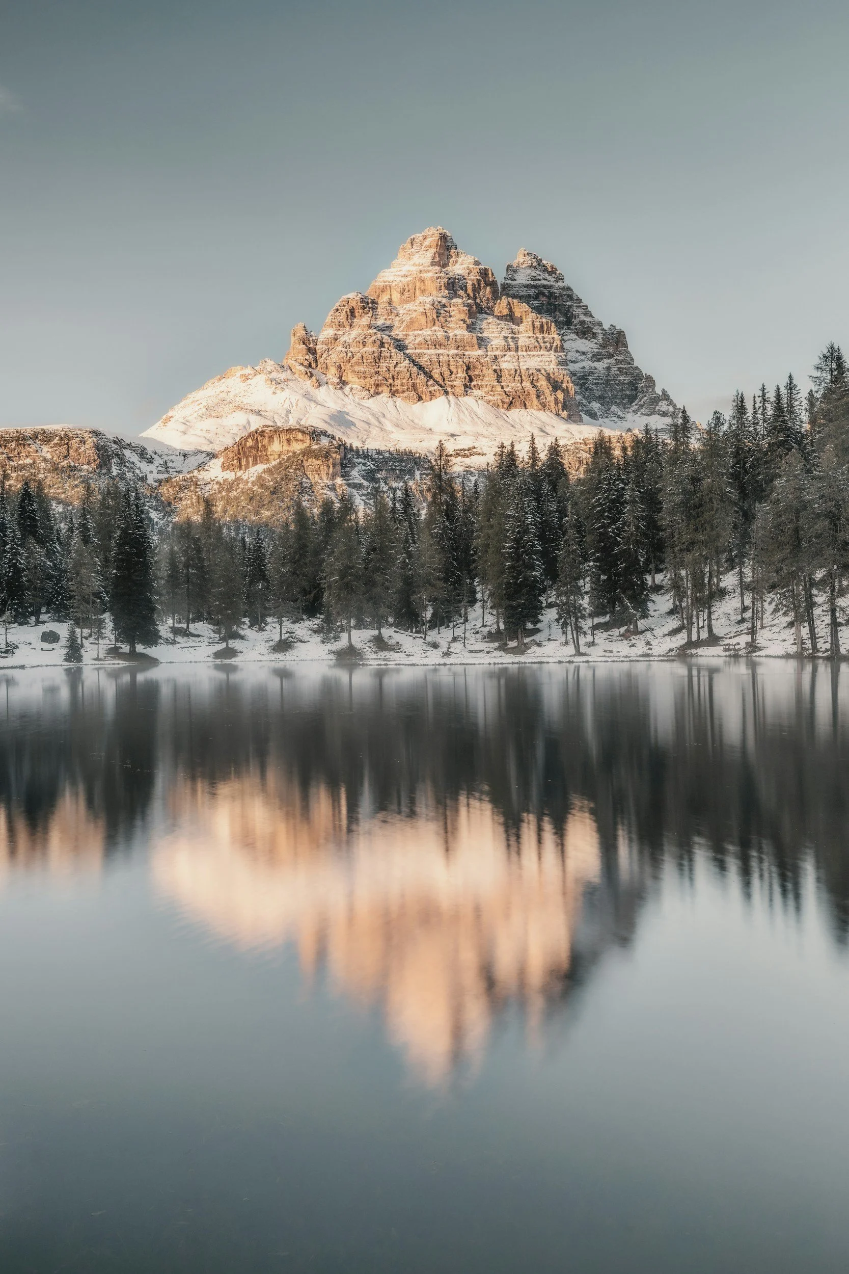 Snow-capped mountains reflected in a calm lake surrounded by pine trees.