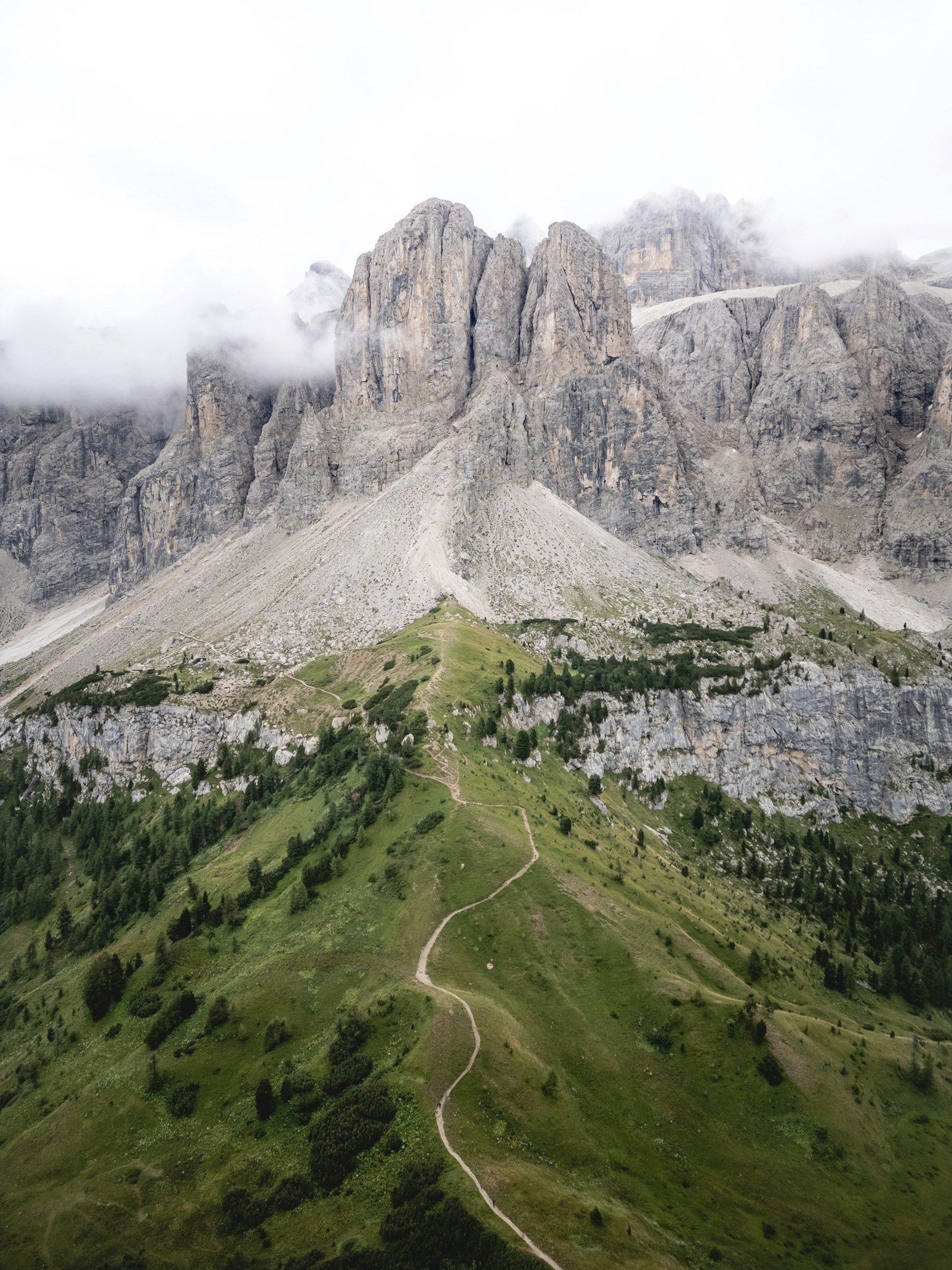 Mountain landscape with rugged peaks partially covered by clouds, green grassy hills with a narrow winding path in the foreground.