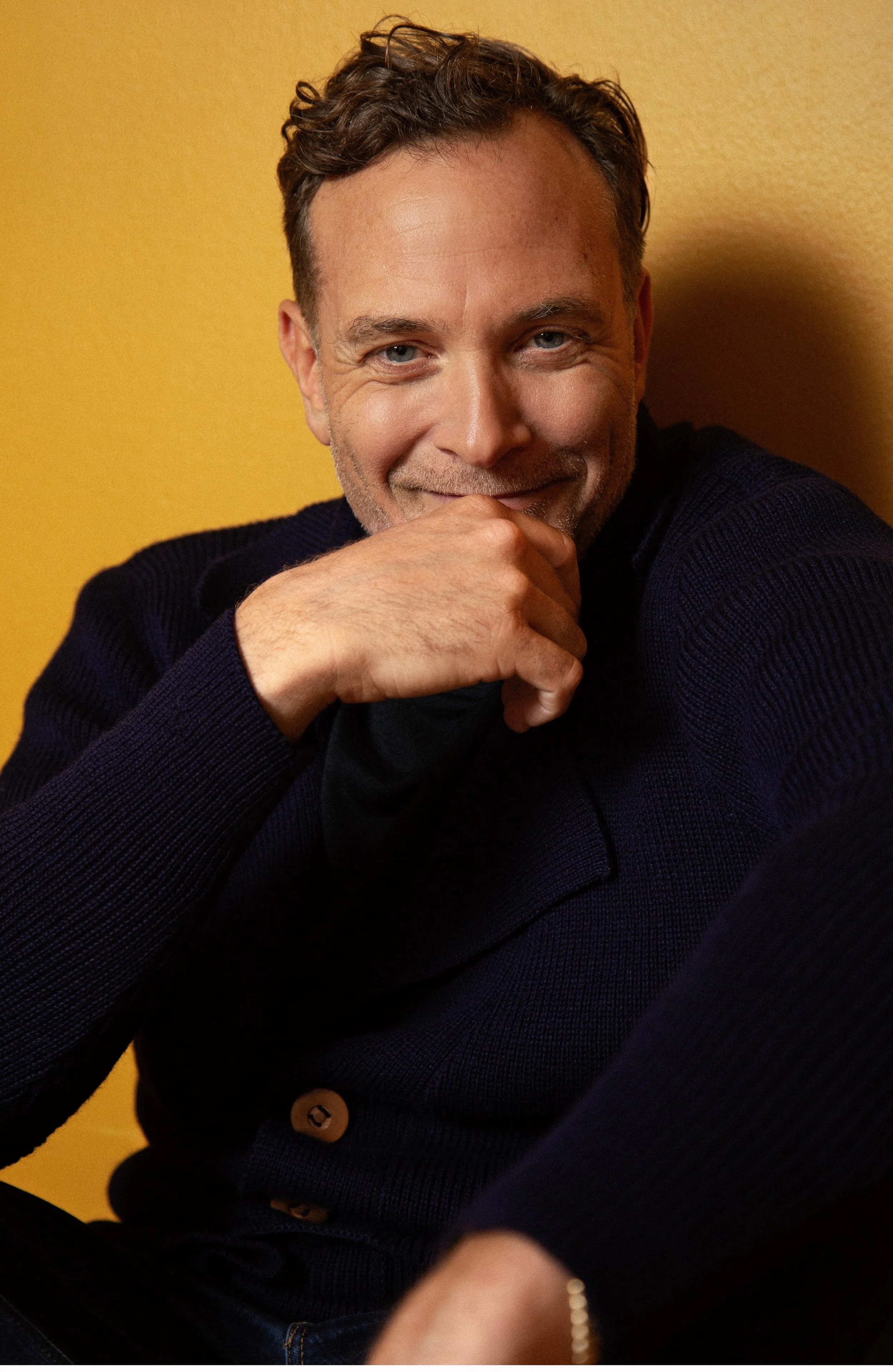 Man wearing yellow tinted glasses and a dark jacket, with short hair and a neutral expression.