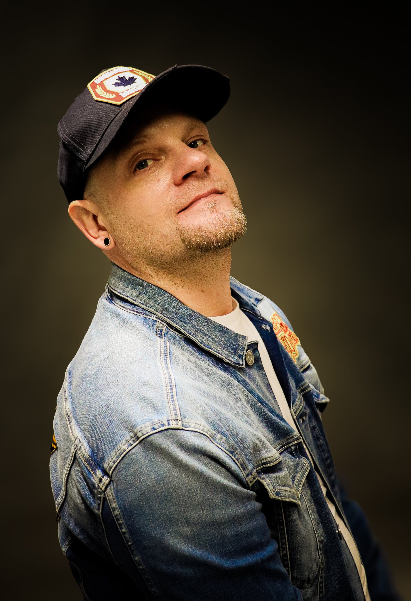 Person wearing a denim jacket and a black cap with star pins, looking to the side.