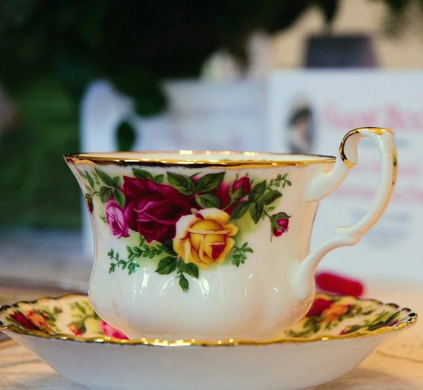 Close-up of a decorative teacup with a floral pattern, gold rim, and ornate handle, placed on a matching saucer with a similar design.