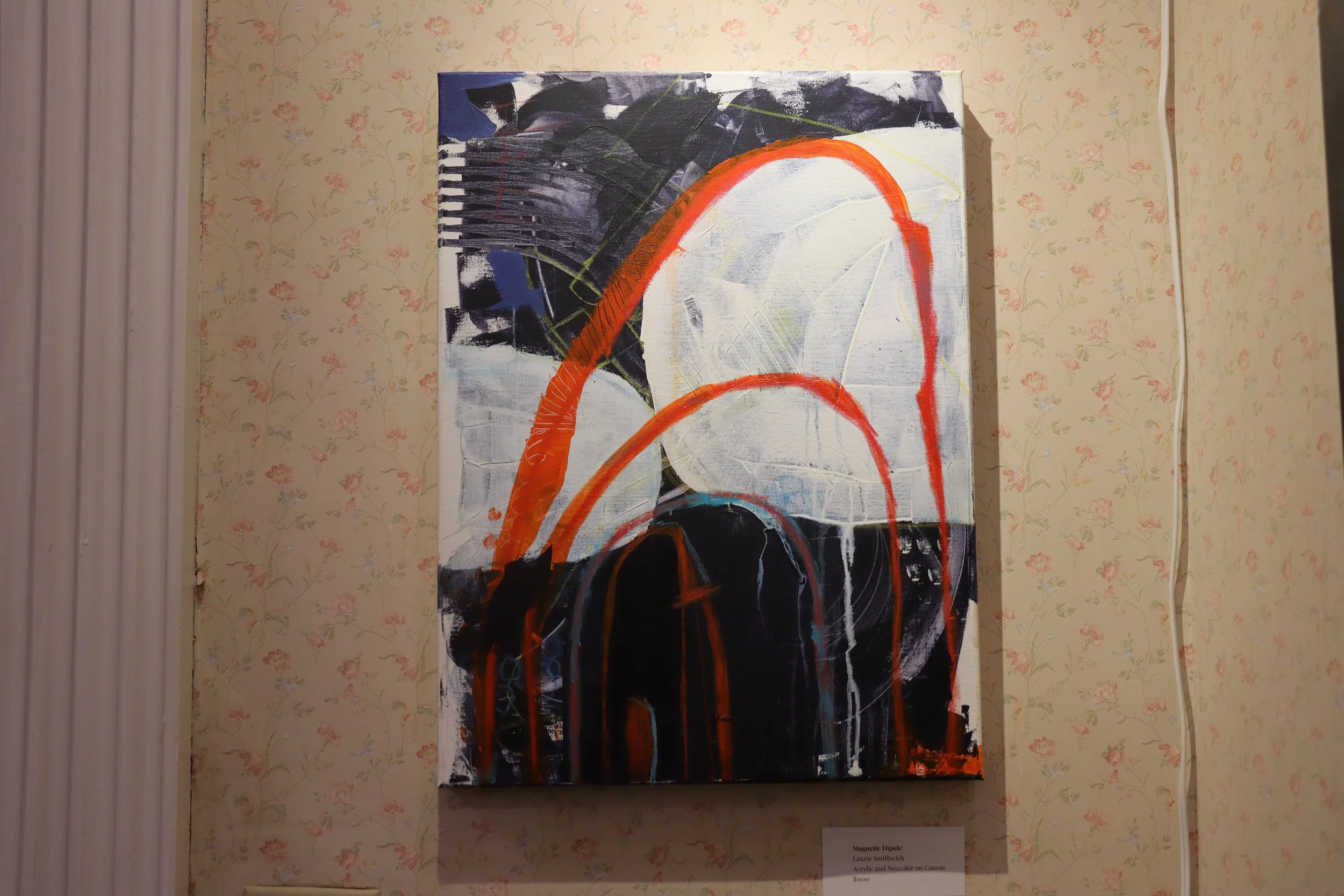 An abstract painting with black, white, orange, and hints of navy blue, featuring curved lines and layered textures, on display against a floral wallpaper background.