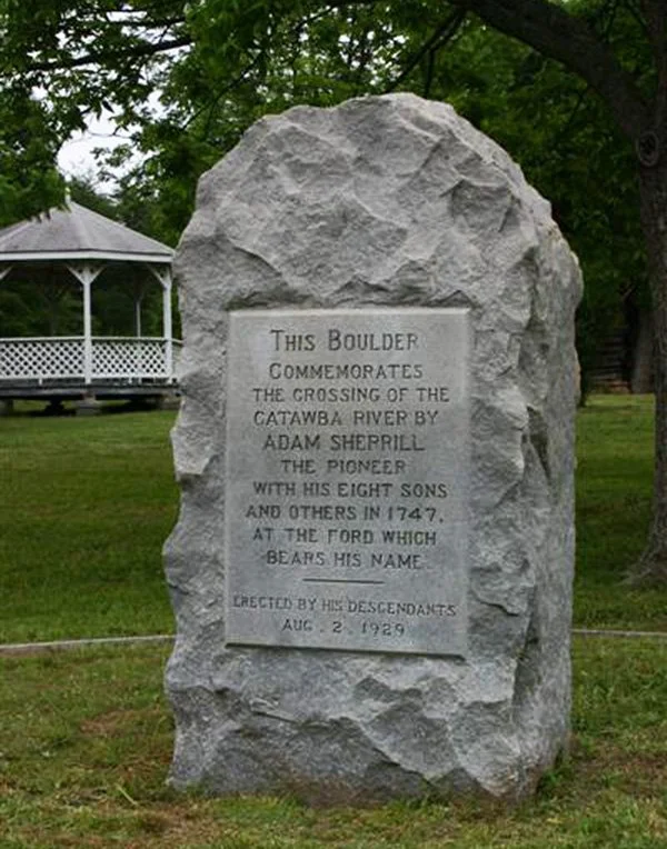 Large stone monument with a carved plaque dedicated to Adam Sherrill, commemorating his crossing of the Catawba River in 1747, located in a park with a gazebo in the background.